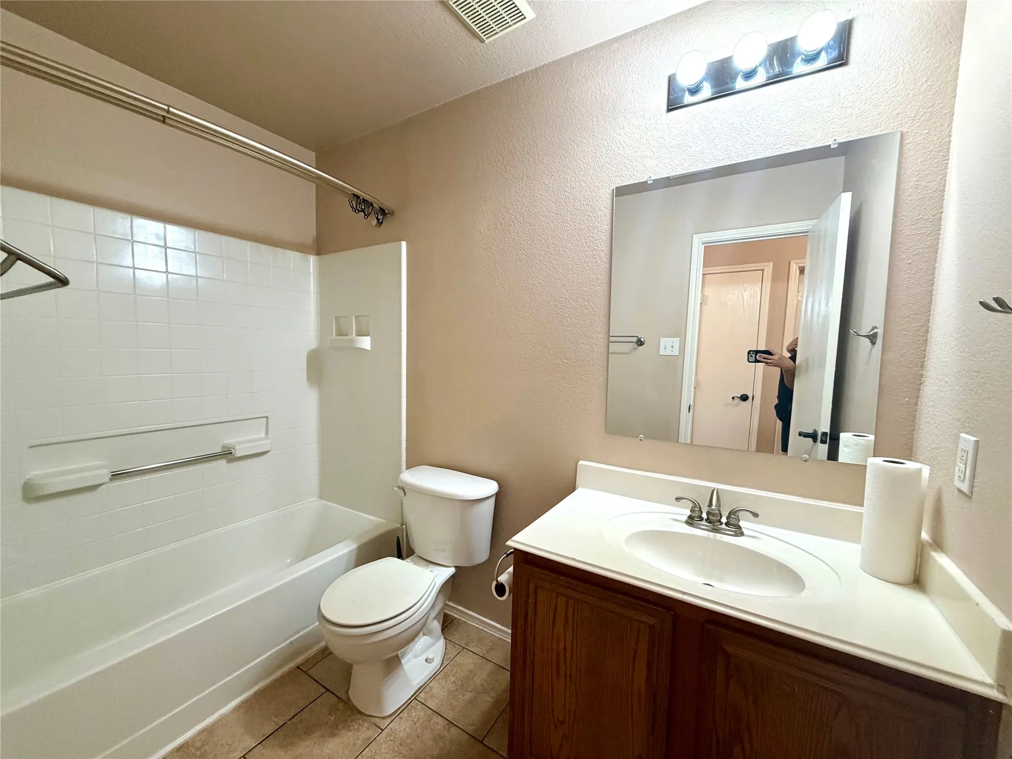 Bathroom featuring wood-finish vanity cabinetry, integrated countertop with oval basin, wall-mounted mirror, three-light fixture, and tub-shower combination with tile-finish surround