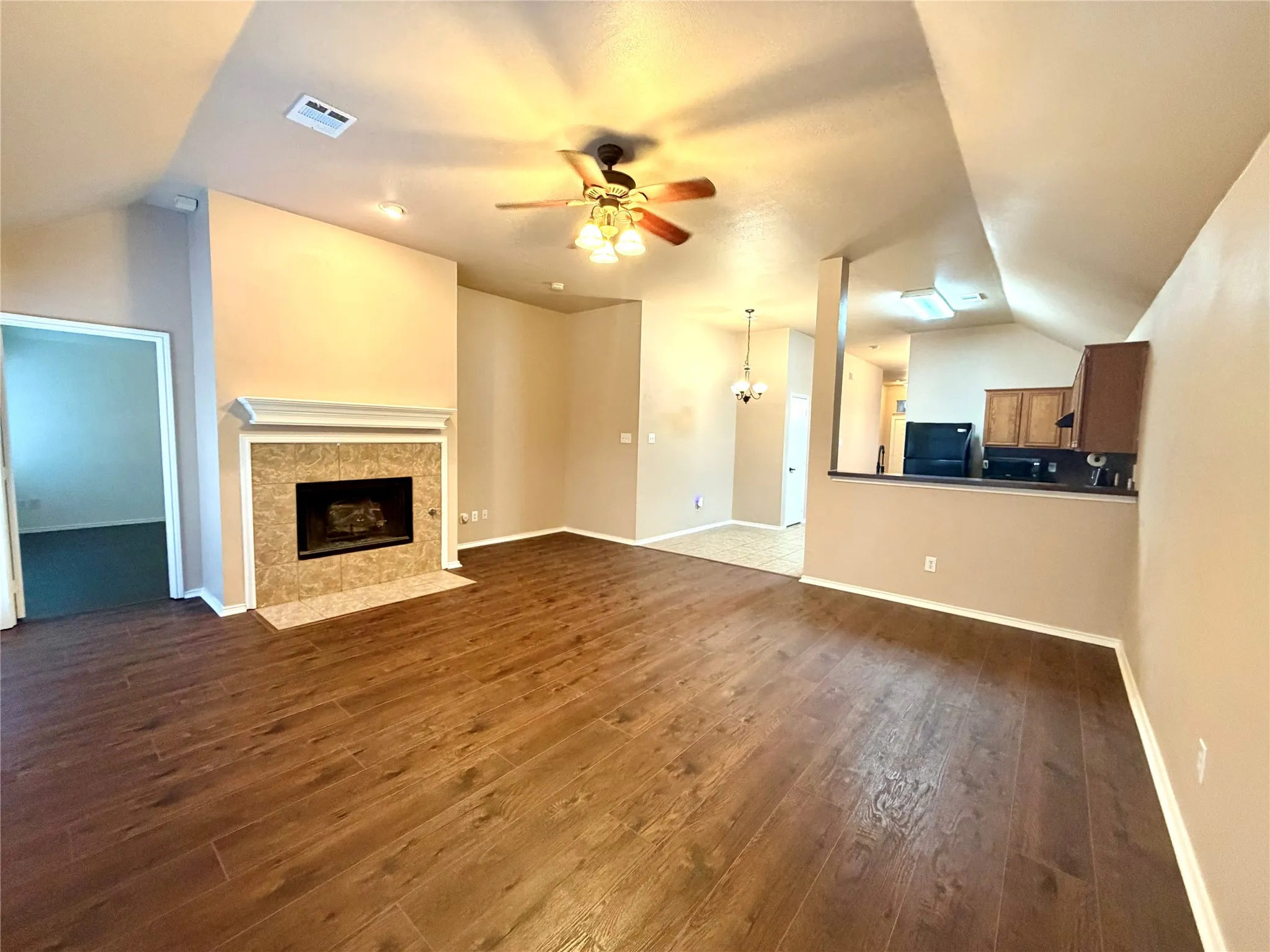 Living area featuring wood-finish flooring, a vaulted ceiling, a fireplace with a tile surround and mantel, and a ceiling fan