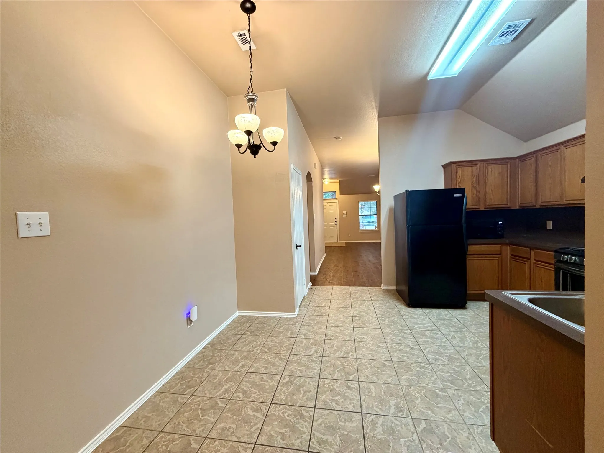 Ceramic tile flooring, stained wood cabinetry, vaulted ceiling with integrated lighting, and three-bulb hanging chandelier