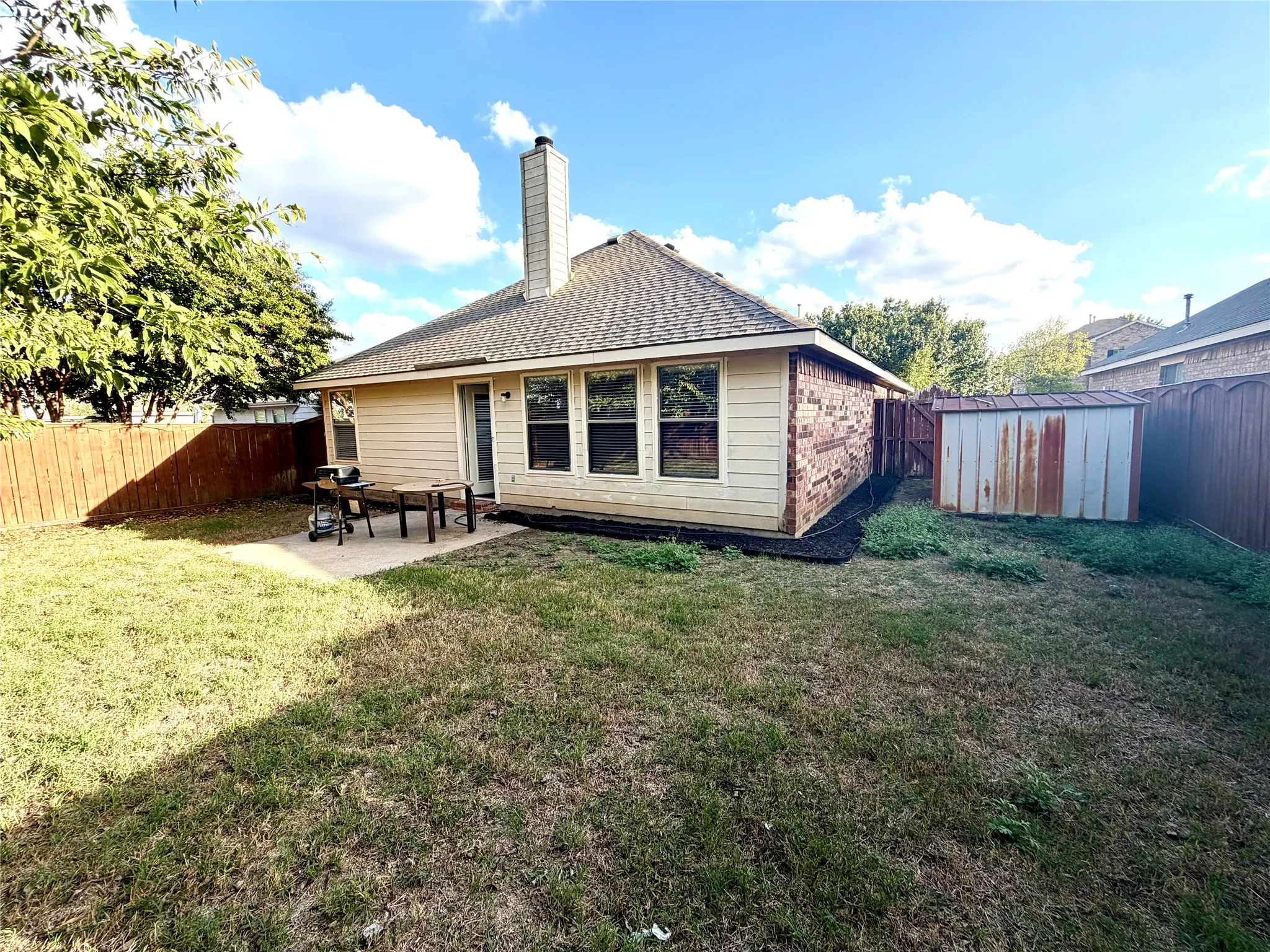 Rear exterior featuring horizontal lap siding, a masonry chimney, a concrete patio, and a fenced backyard with an exterior storage structure