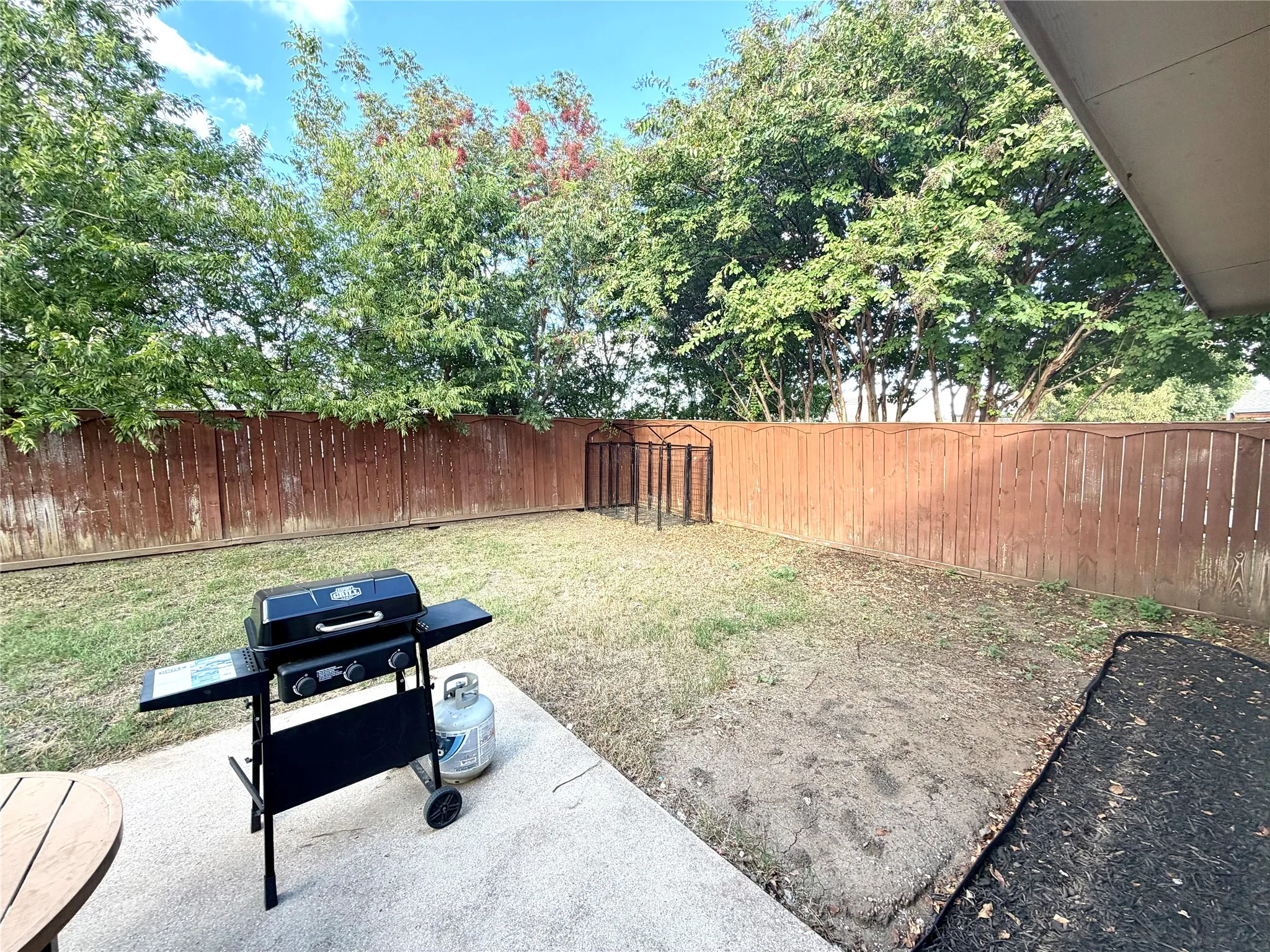 Rear yard featuring a concrete patio, perimeter wood fencing, and mature trees