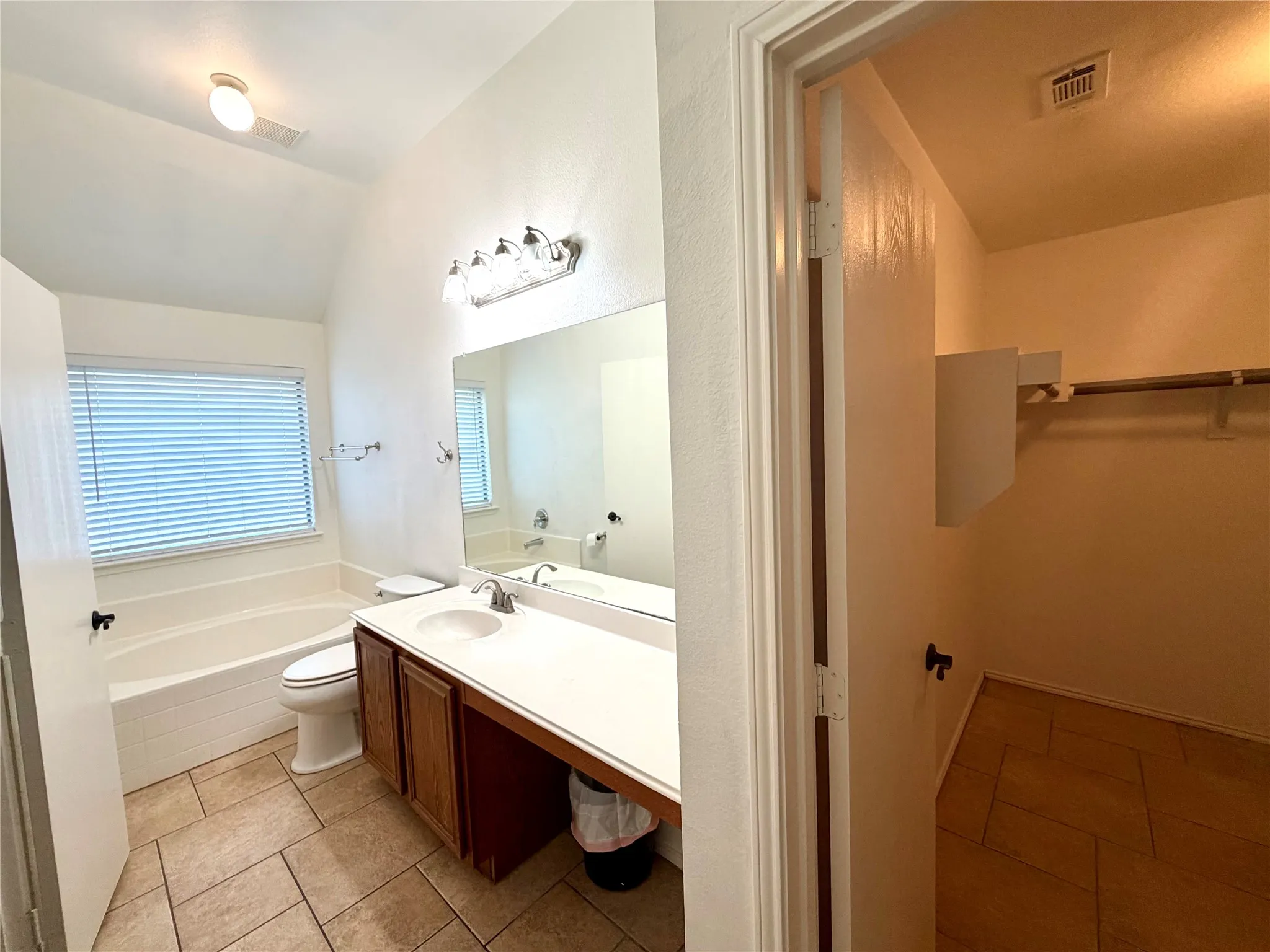 Bathroom featuring tile flooring, a soaking tub with a tiled surround, a vanity with a solid-surface countertop, and an attached walk-in closet with built-in shelving