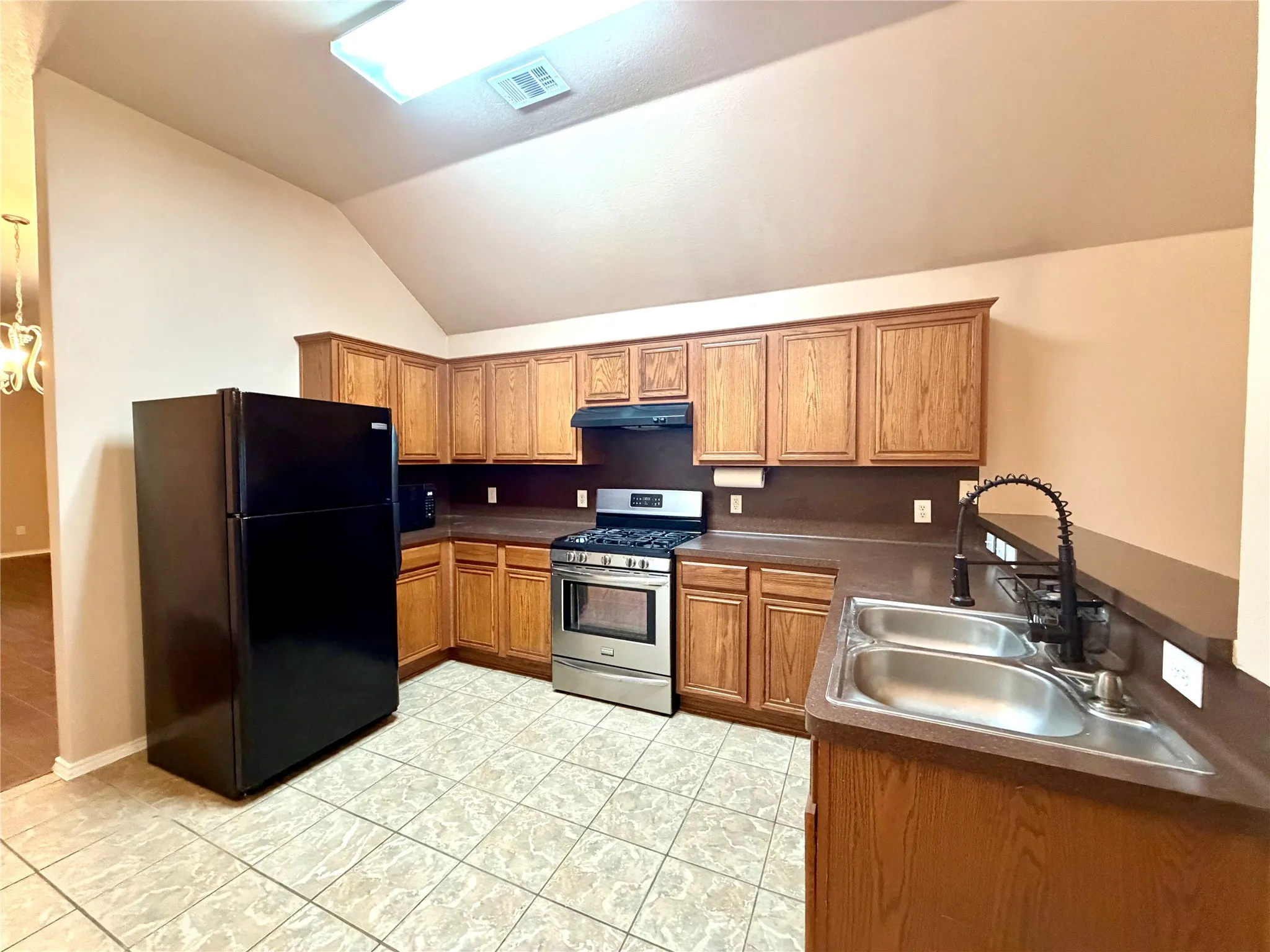 Kitchen featuring wood cabinetry, vaulted ceiling, double-basin stainless steel sink with matte black faucet, and stainless steel gas range
