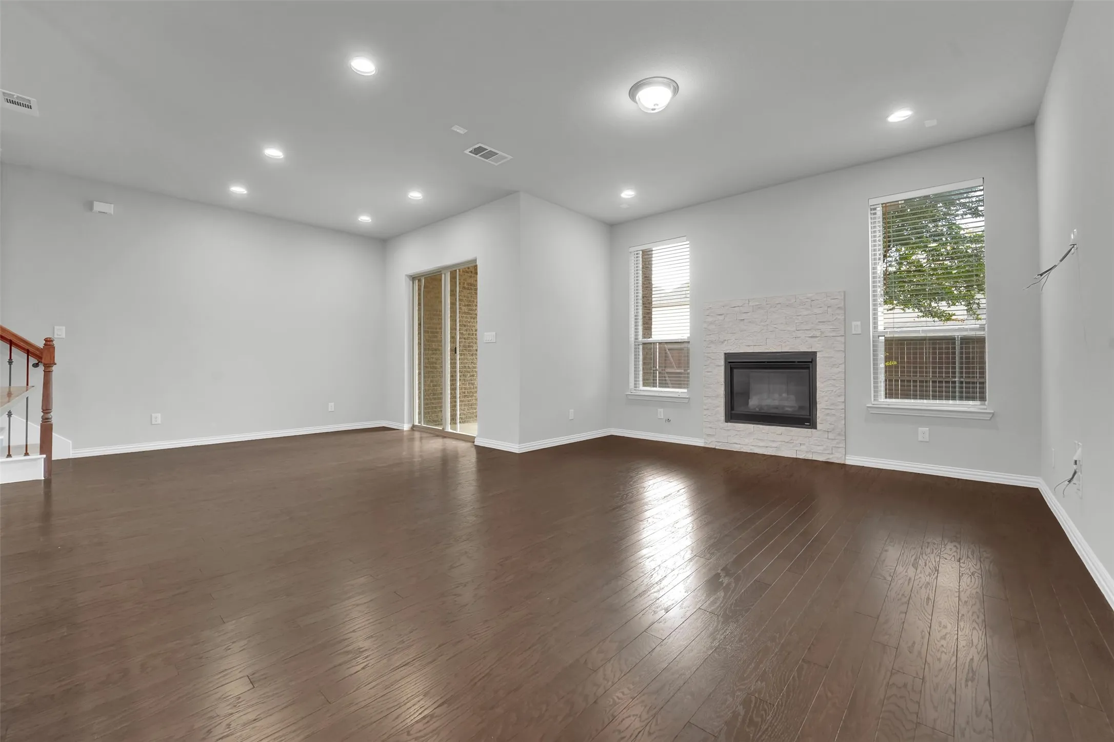 Spacious living area featuring wood-finish flooring, recessed lighting, and a fireplace with a textured stone surround