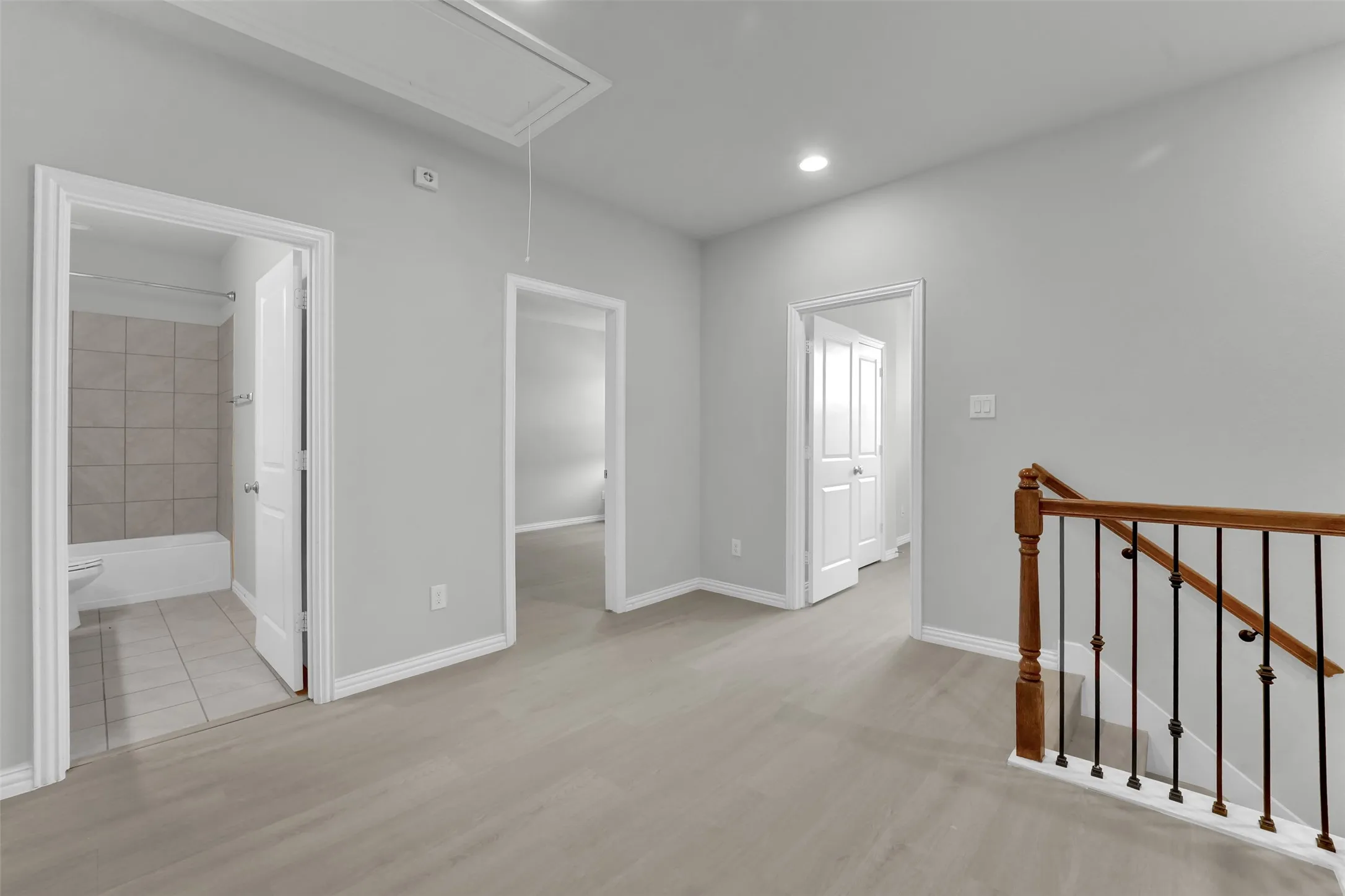 Light gray wood-finish flooring, recessed lighting, white trim, and a staircase with wood handrails and black metal balusters