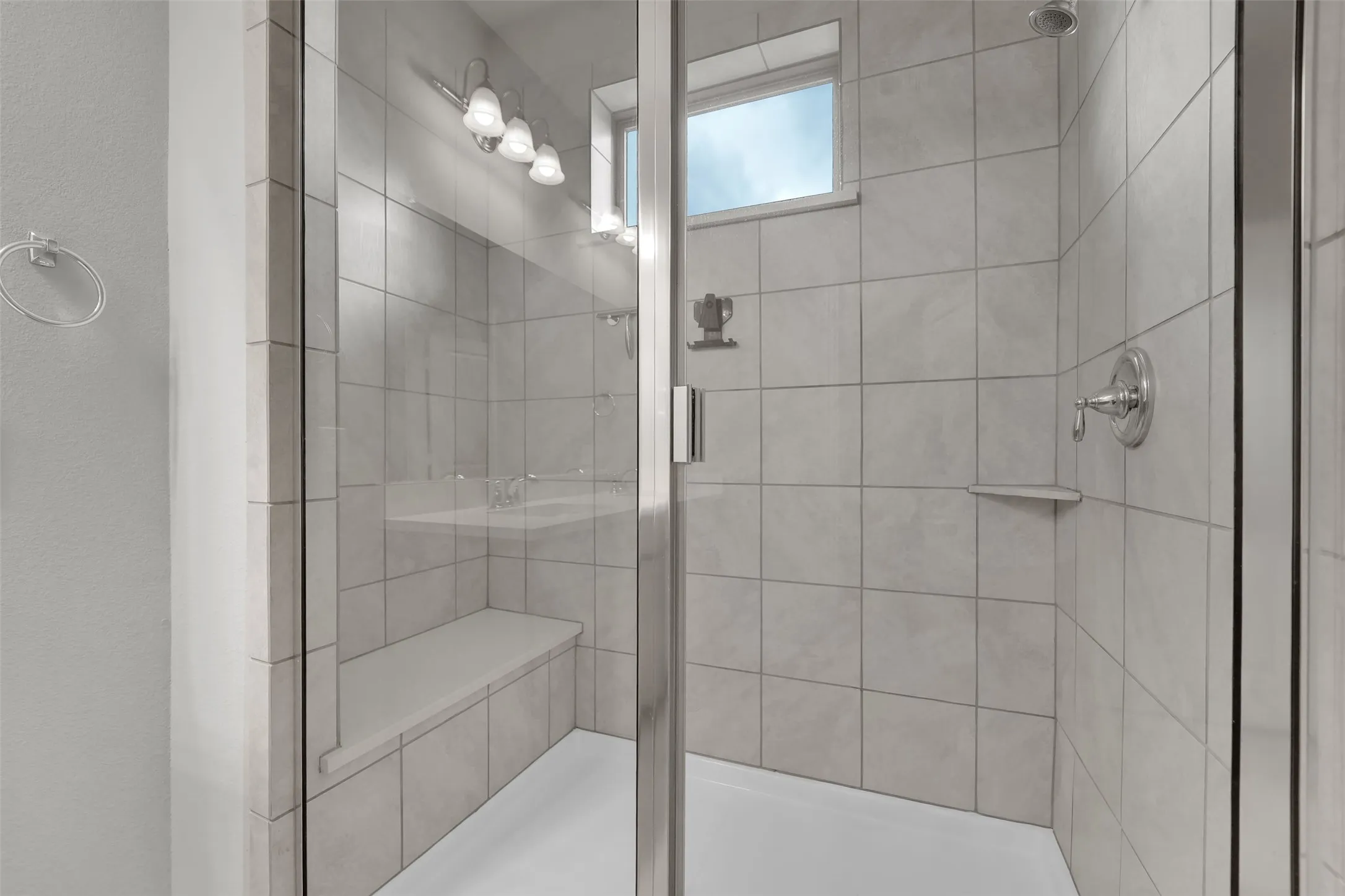 Glass-enclosed shower with tile surround, built-in bench, and chrome fixtures
