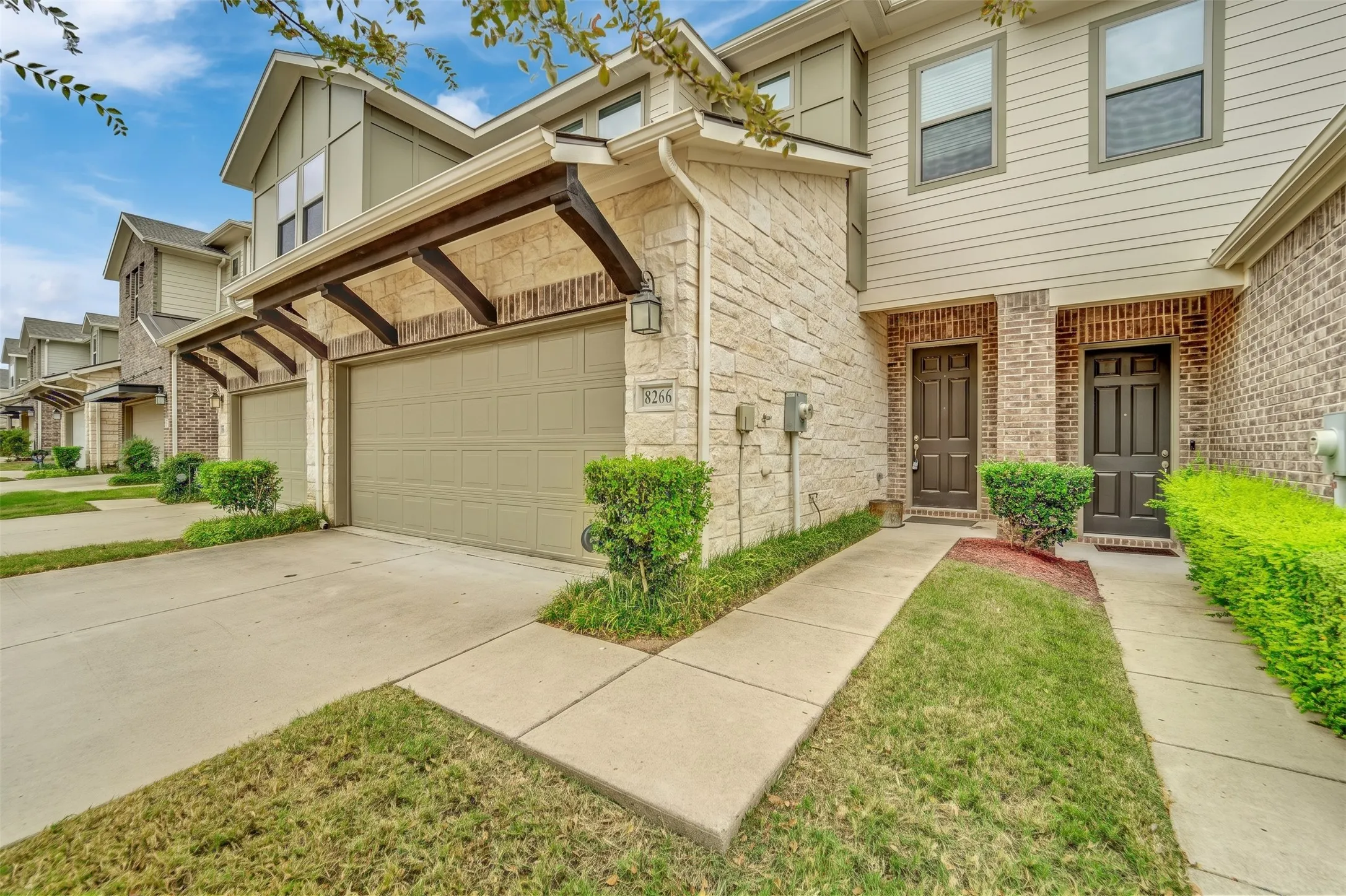 Exterior featuring stone and brick accents, an attached two-car garage with a pergola-style awning, and an entry with a dark panel door