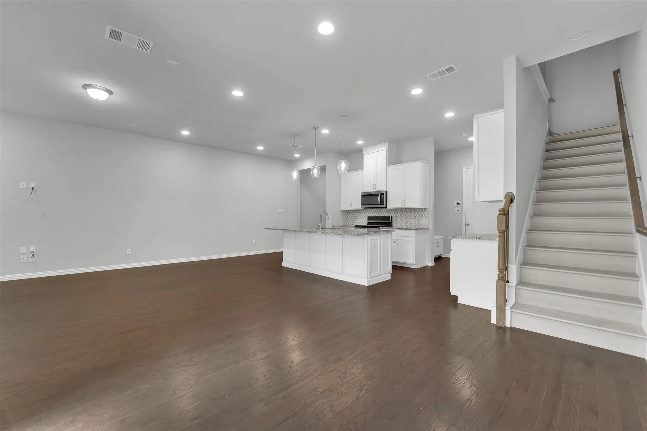 Open-concept living area featuring wood-finish flooring, recessed lighting, and a modern kitchen with white cabinetry, stainless steel appliances, and a tiled backsplash