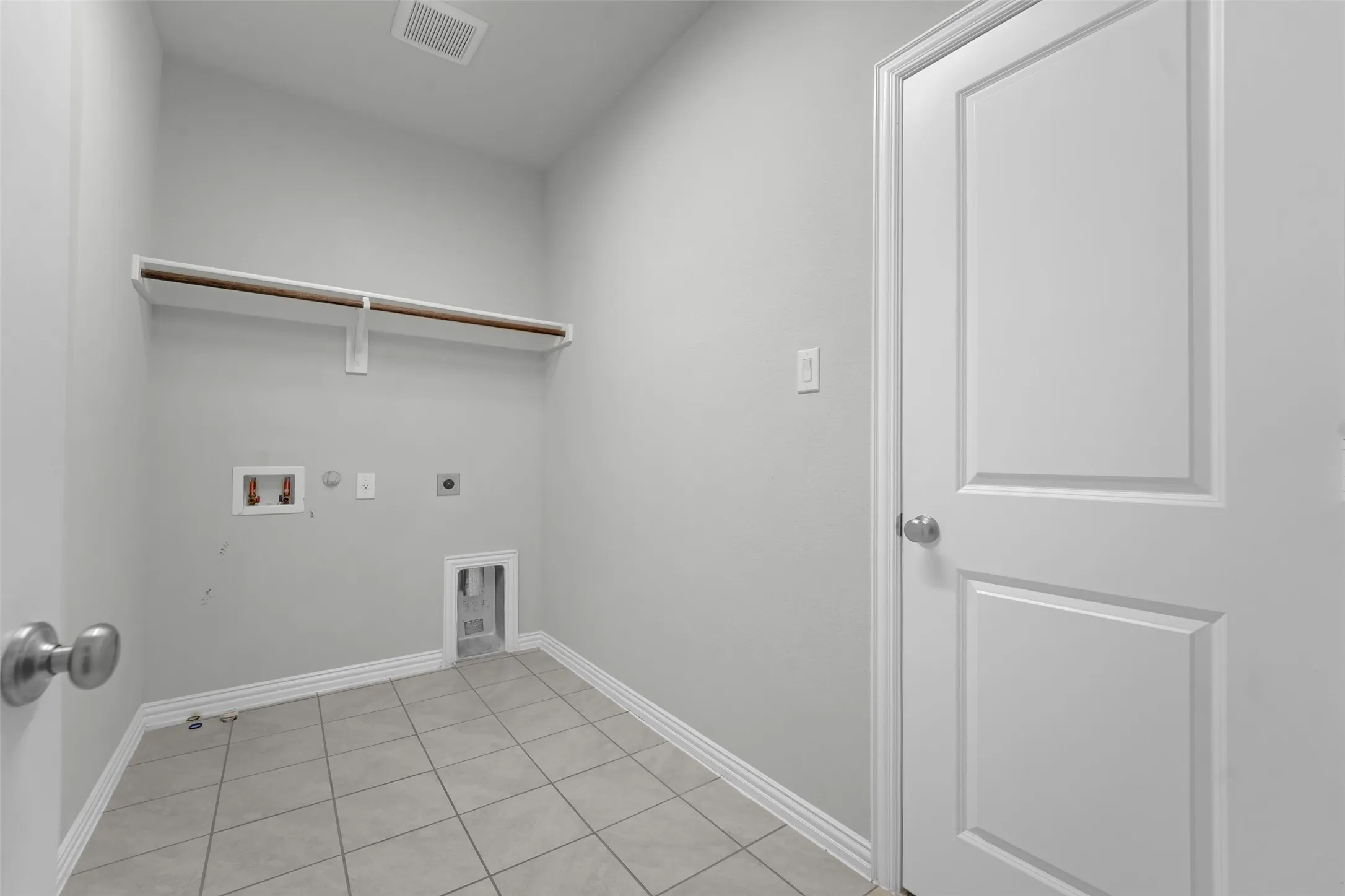 Utility room featuring a built-in shelf with a hanging rod, tile flooring, and light gray wall paint