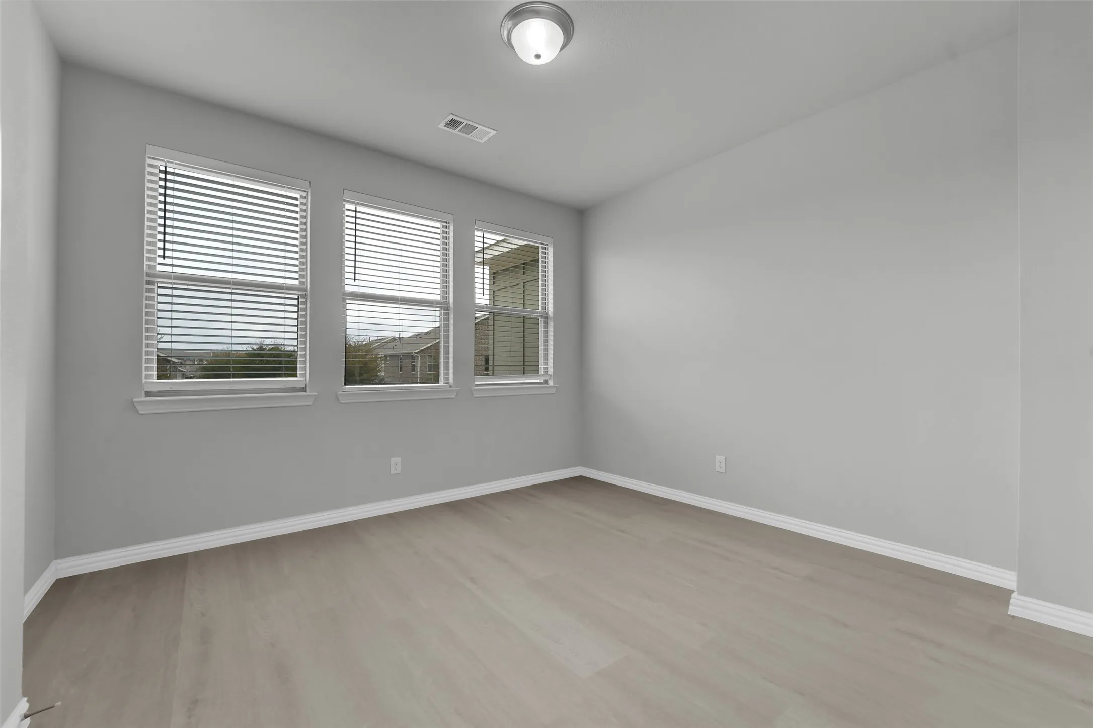 Light gray wood-finish flooring, multiple windows with blinds, and flush-mount ceiling light