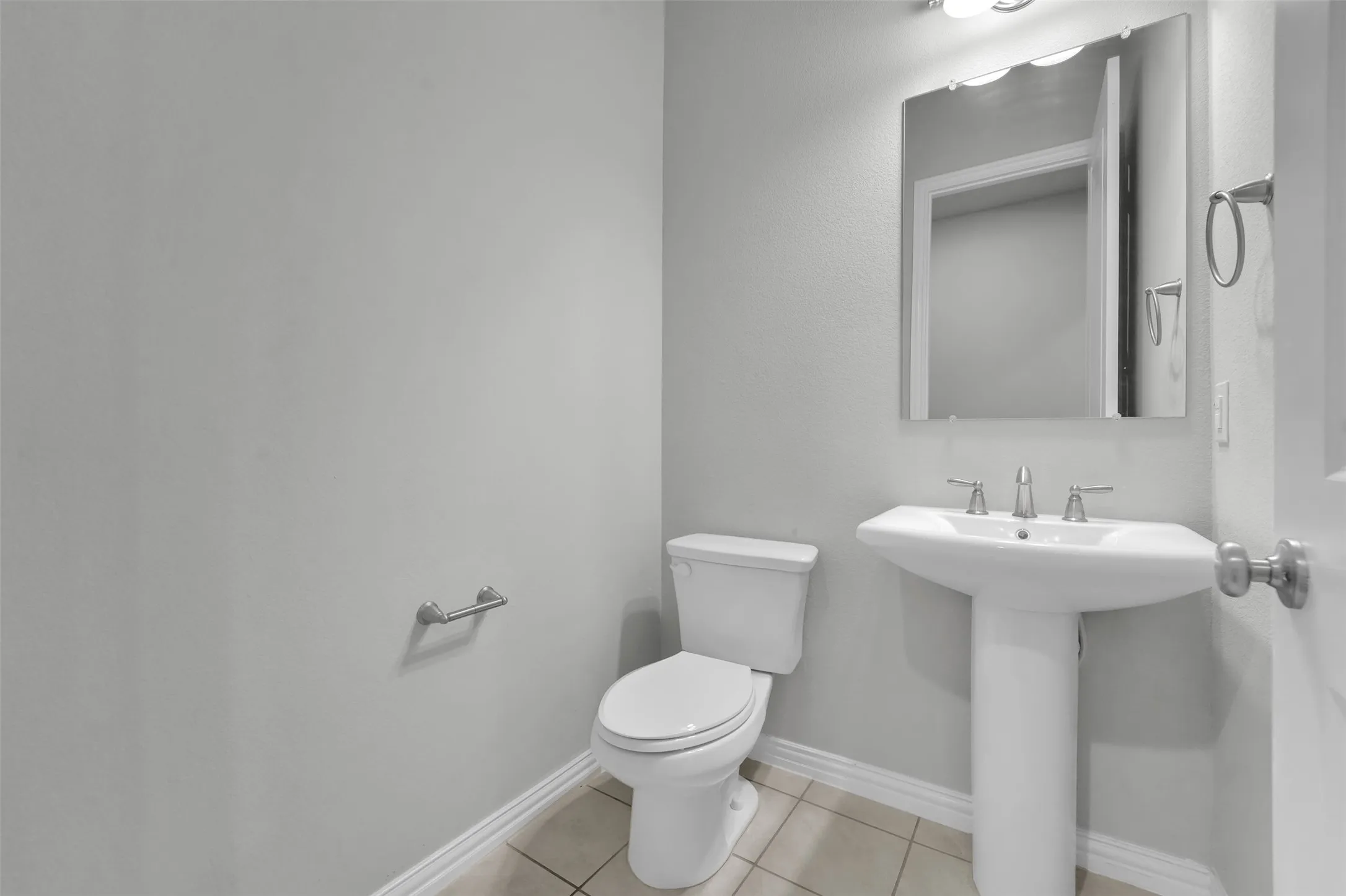 Pedestal sink with chrome faucet, wall-mounted mirror, and tile flooring