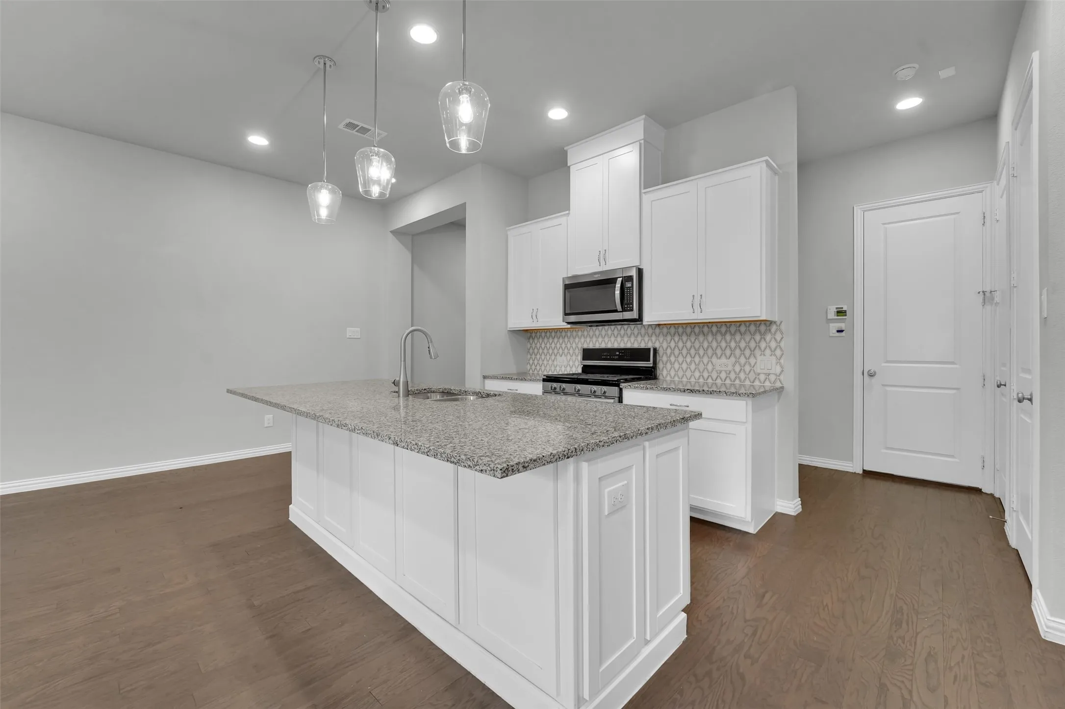 Kitchen featuring wood-finish flooring, a central island with a stone countertop, pendant lighting, white cabinetry, and a patterned tile backsplash