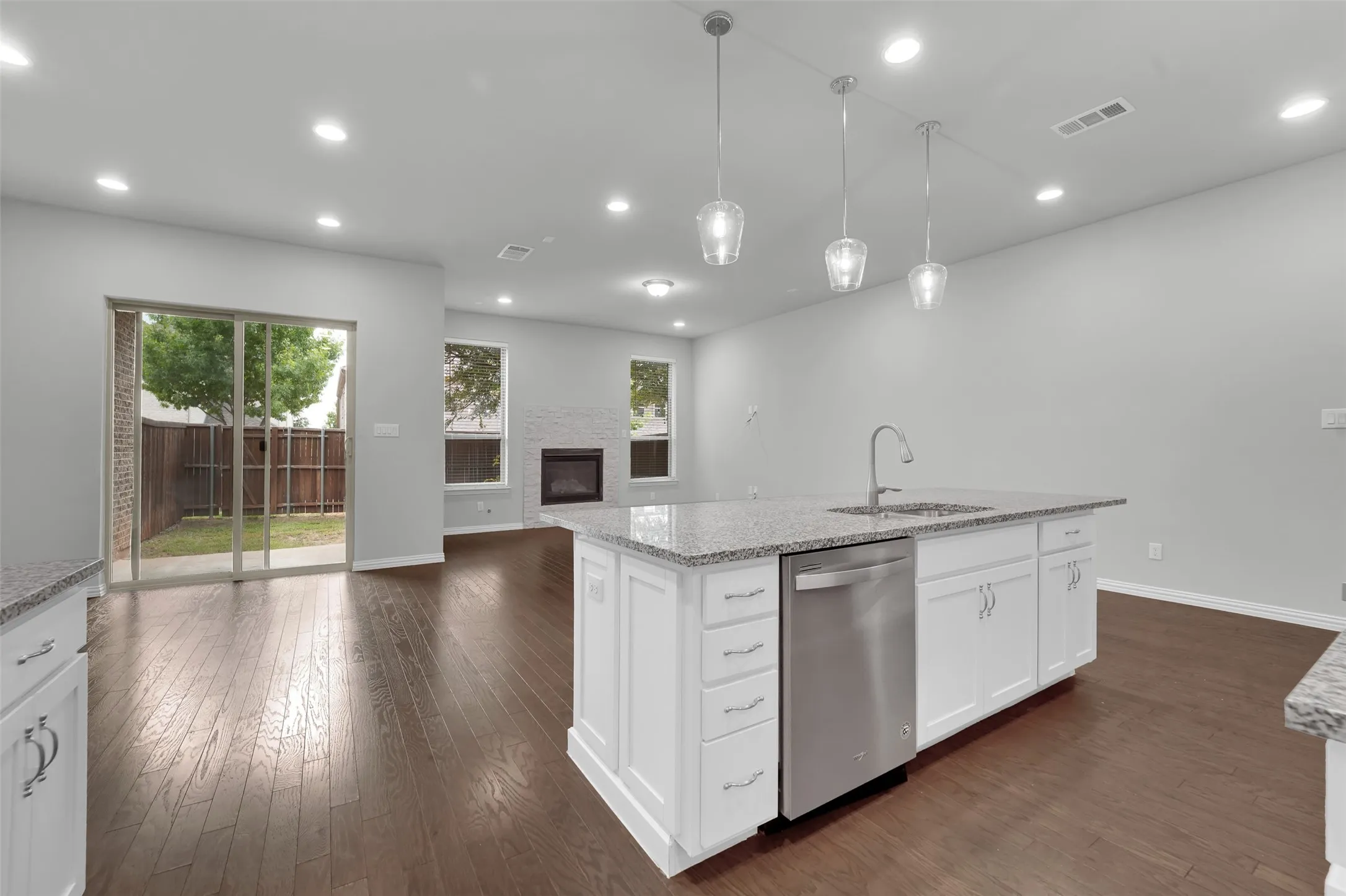 Open-concept living space with dark wood-finish flooring, white shaker cabinetry, an island with a stainless steel sink and dishwasher, and recessed lighting