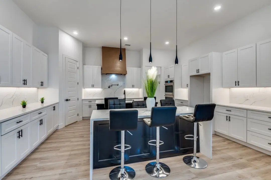 Kitchen featuring white shaker-style cabinetry, a contrasting dark-toned kitchen island with a stone-finish countertop, a custom wood-finish range hood, under-cabinet lighting, and recessed ceiling lighting