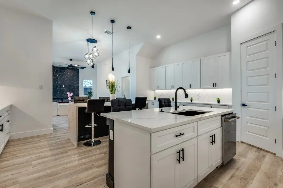 Kitchen featuring a central island with a quartz countertop, white shaker-style cabinetry, matte black hardware, integrated stainless steel dishwasher, and wood-finish flooring