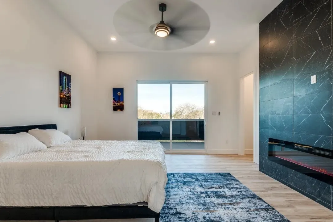 Floor-to-ceiling dark stone fireplace surround with integrated linear firebox, wood-finish flooring, recessed lighting, ceiling fan with integrated light, and sliding glass door