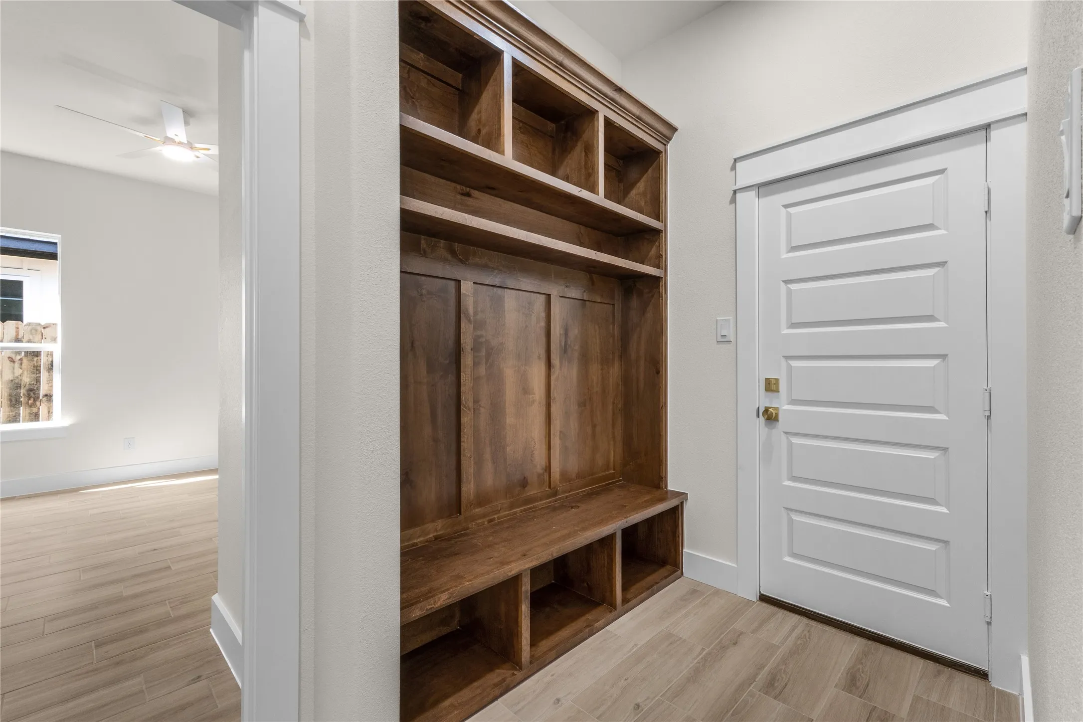Built-in wooden mudroom cabinetry featuring upper cubbies, paneled backing, and lower open shelving, complemented by wood-finish tile flooring and a five-panel interior door