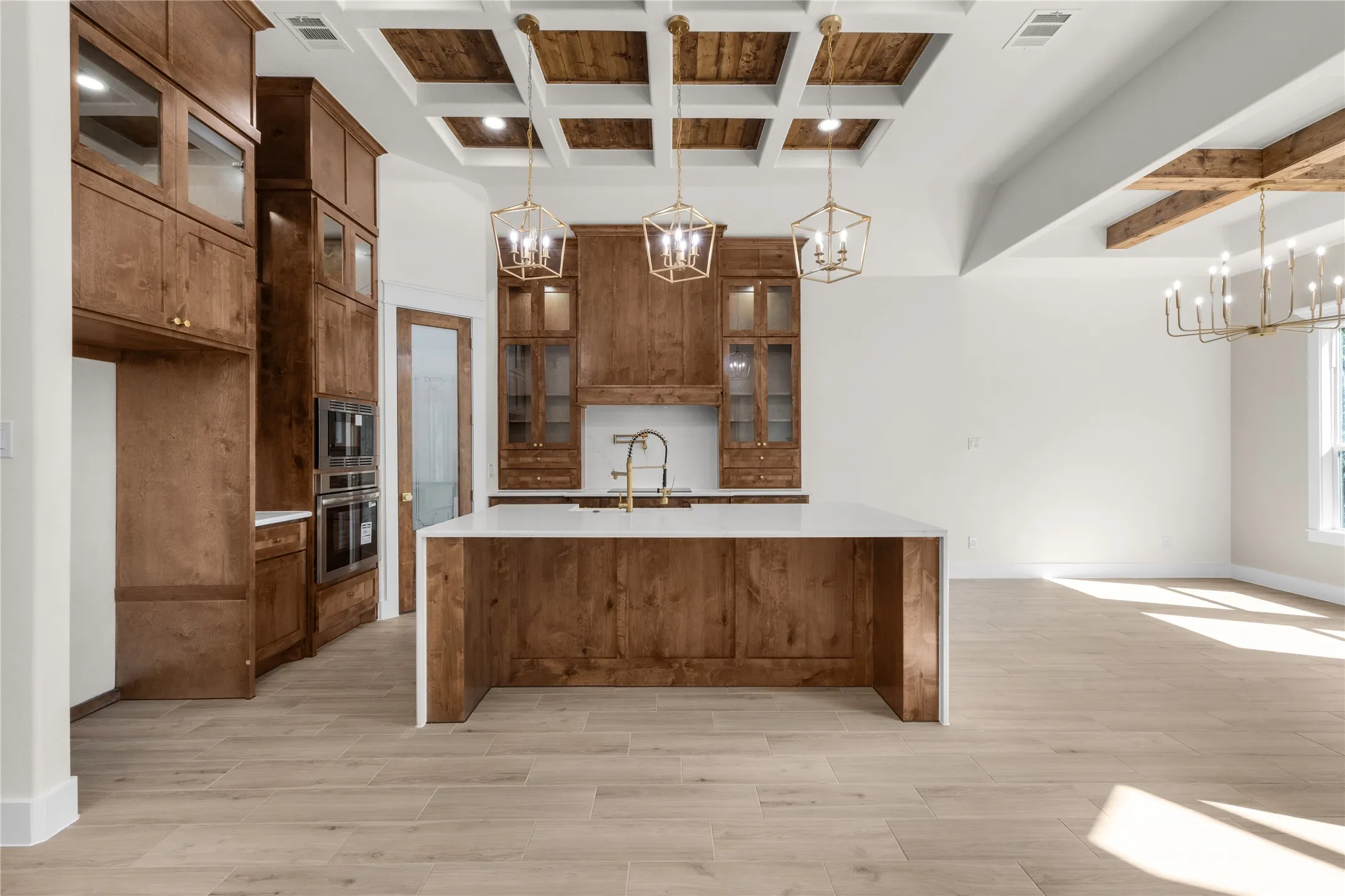 Kitchen featuring custom wood cabinetry, a central island with a solid surface countertop, coffered ceiling with wood accents, geometric pendant lighting, and wood-finish flooring