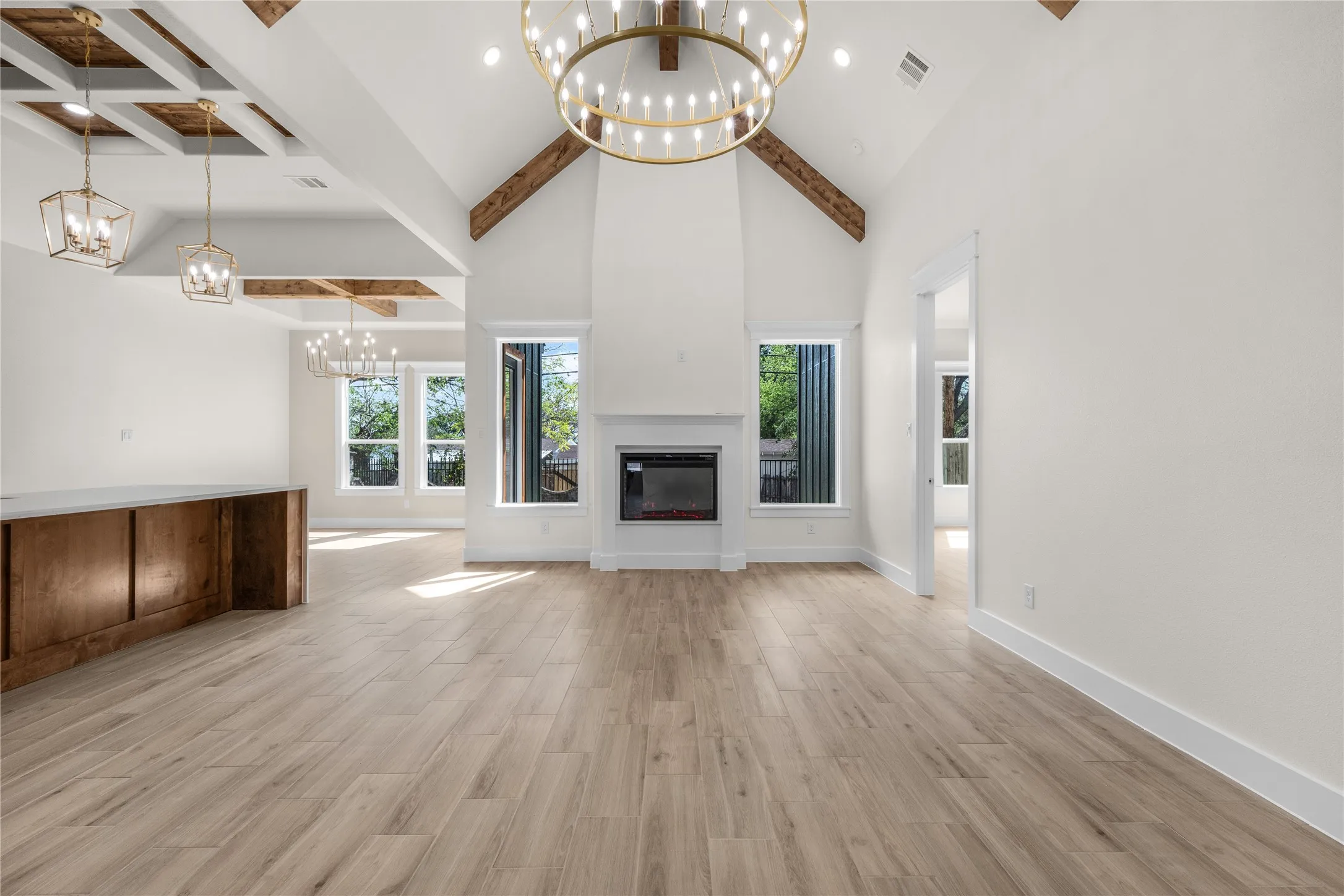 Vaulted ceiling featuring exposed wood beams, a central fireplace, wood-finish flooring, and decorative chandeliers