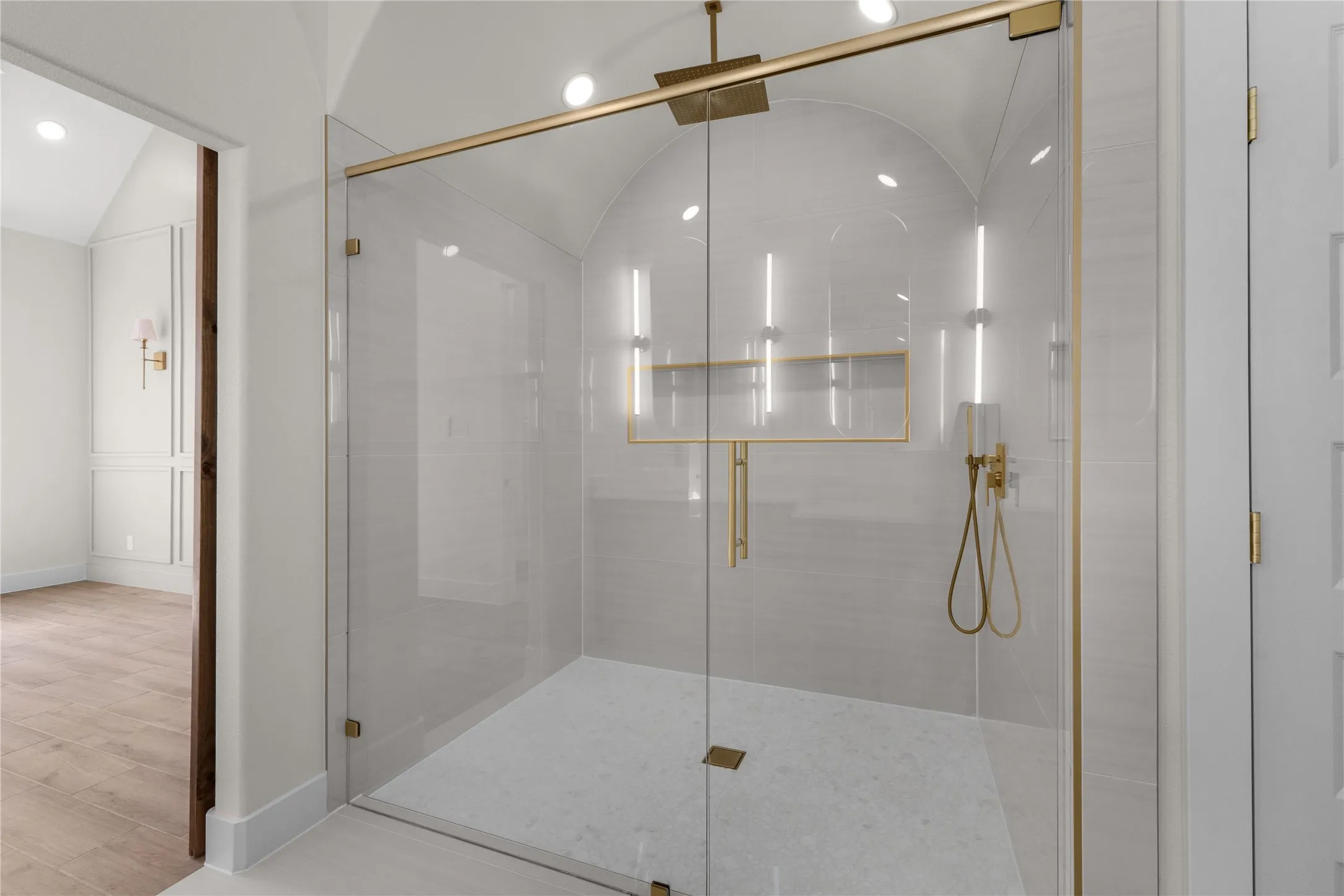 Walk-in shower featuring an arched ceiling, floor-to-ceiling tile surround, gold-finish hardware, a rainfall shower head with handheld sprayer, and a built-in recessed niche