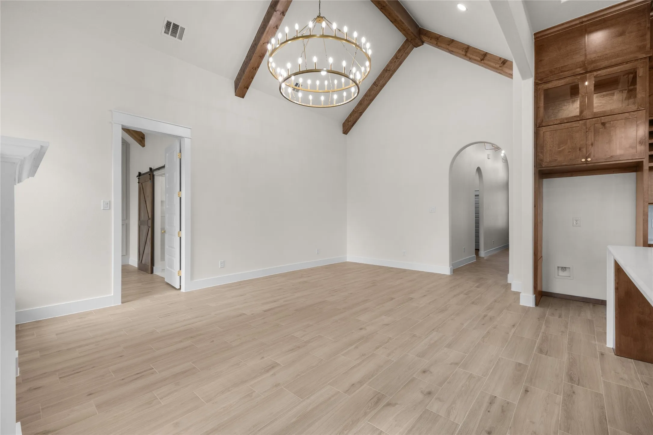 Vaulted ceilings with exposed wood beams, circular tiered chandelier, wood-finish flooring, floor-to-ceiling custom wood cabinetry, and arched doorways