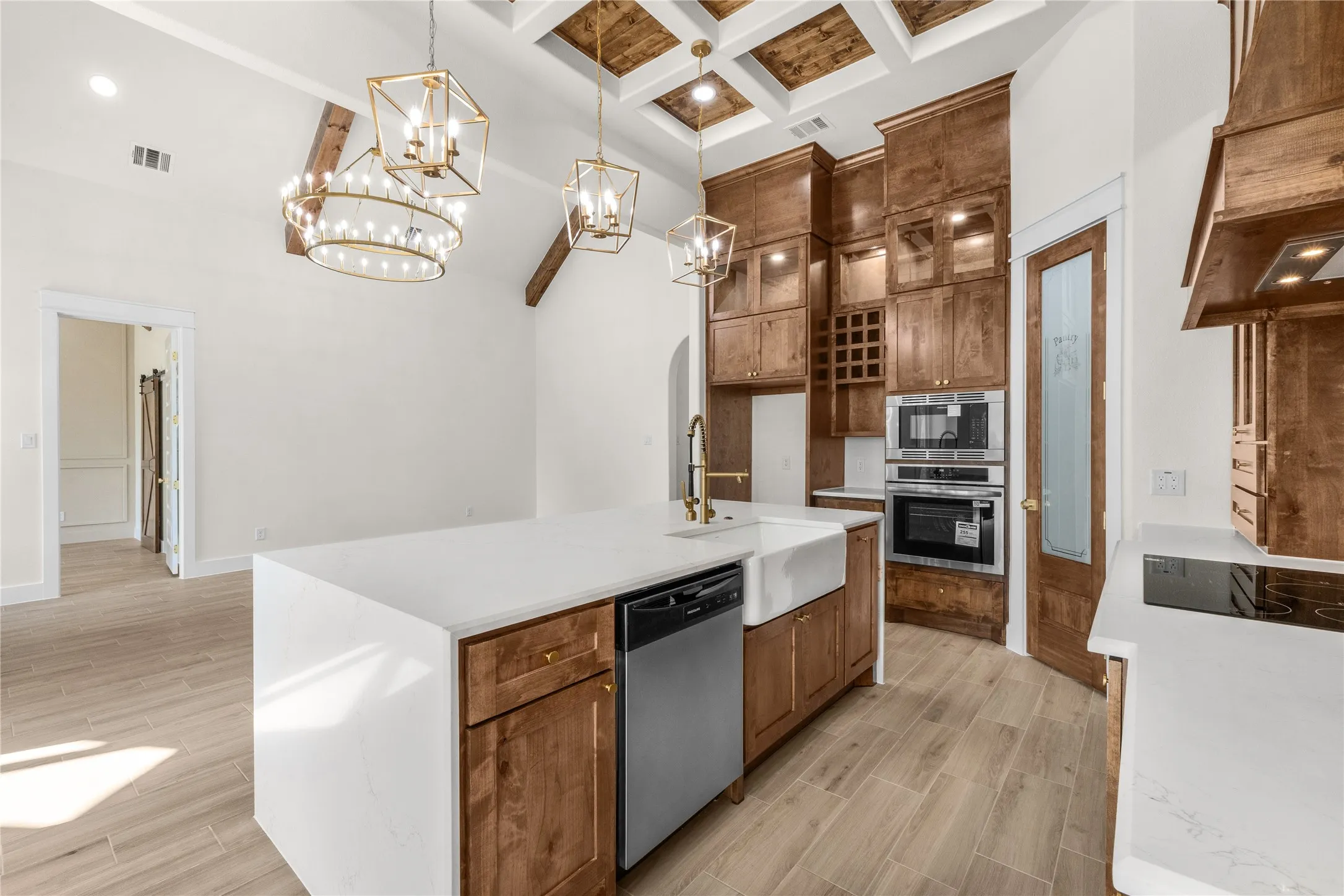 Kitchen featuring wood-finish flooring, coffered ceiling with inset wood paneling, wood cabinetry with integrated wine storage, quartz countertops, and an island with an apron-front sink