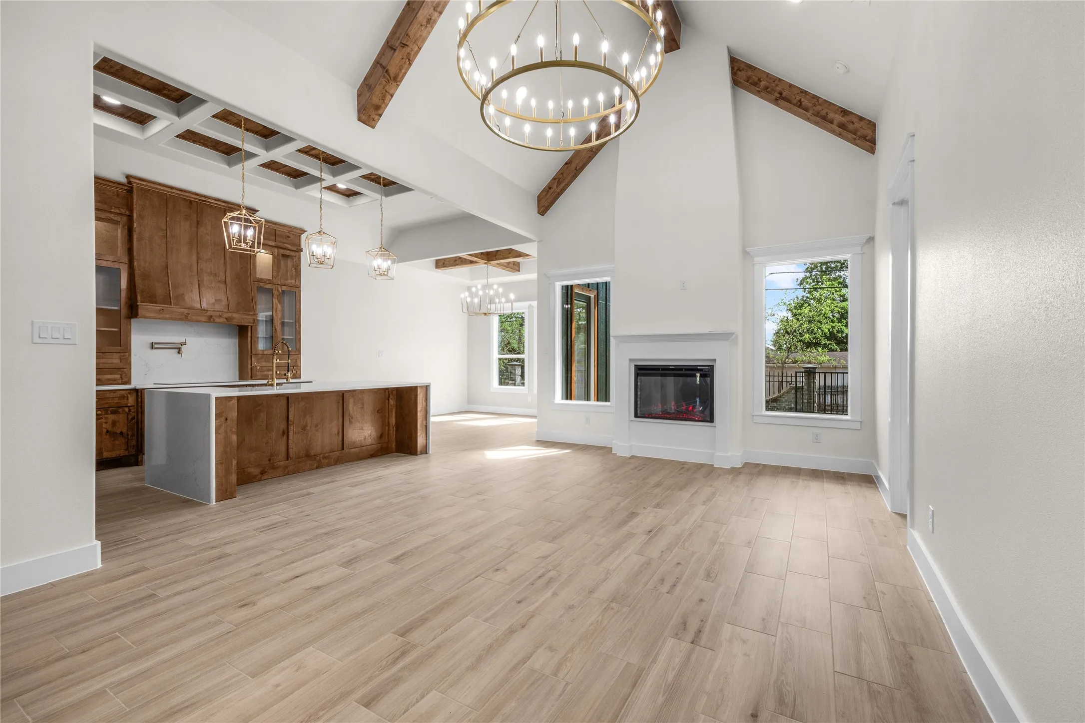 Vaulted ceilings with exposed wooden beams, wood-finish flooring, custom wooden cabinetry, a built-in fireplace, and expansive custom chandeliers