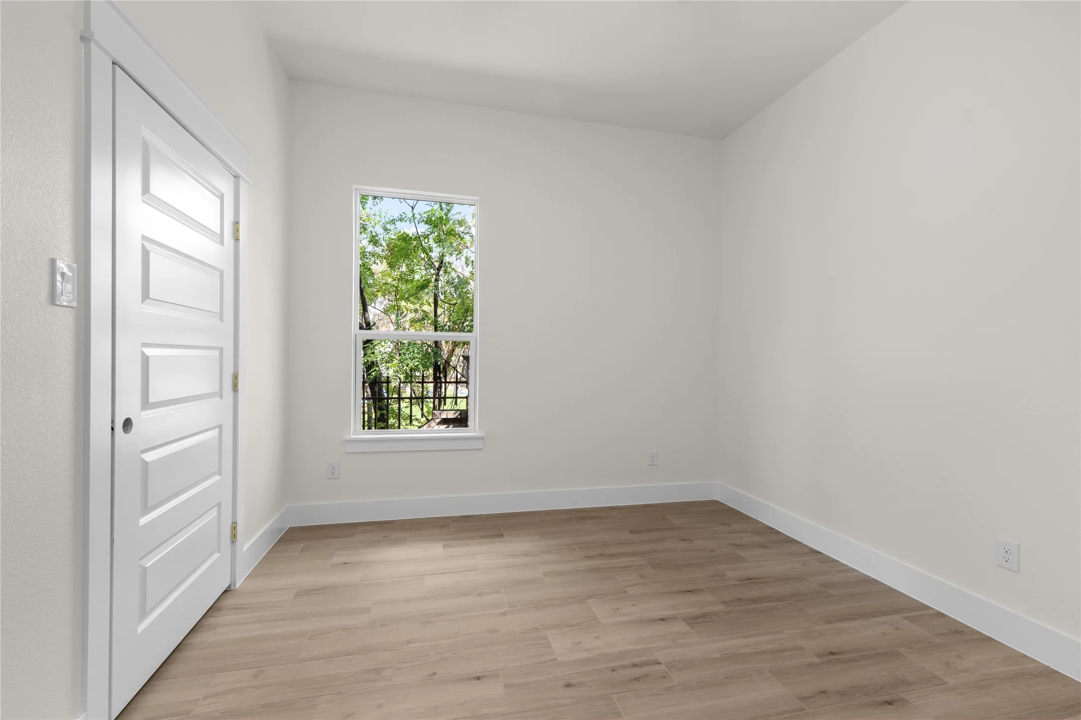 Neutral-toned interior space featuring wood-finish flooring, a single-hung window, and a white five-panel interior door