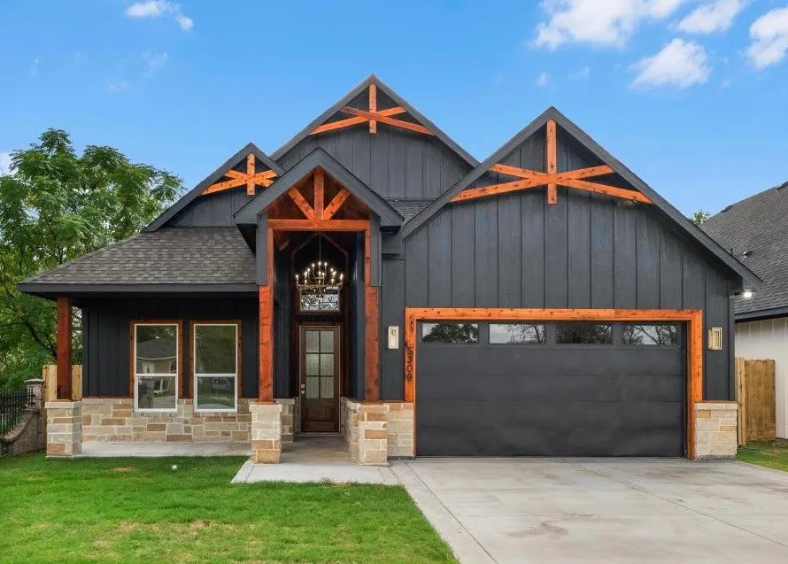 Modern farmhouse exterior featuring vertical dark siding, wood-toned timber accents, natural stone masonry, an integrated garage with transom windows, and a covered entryway