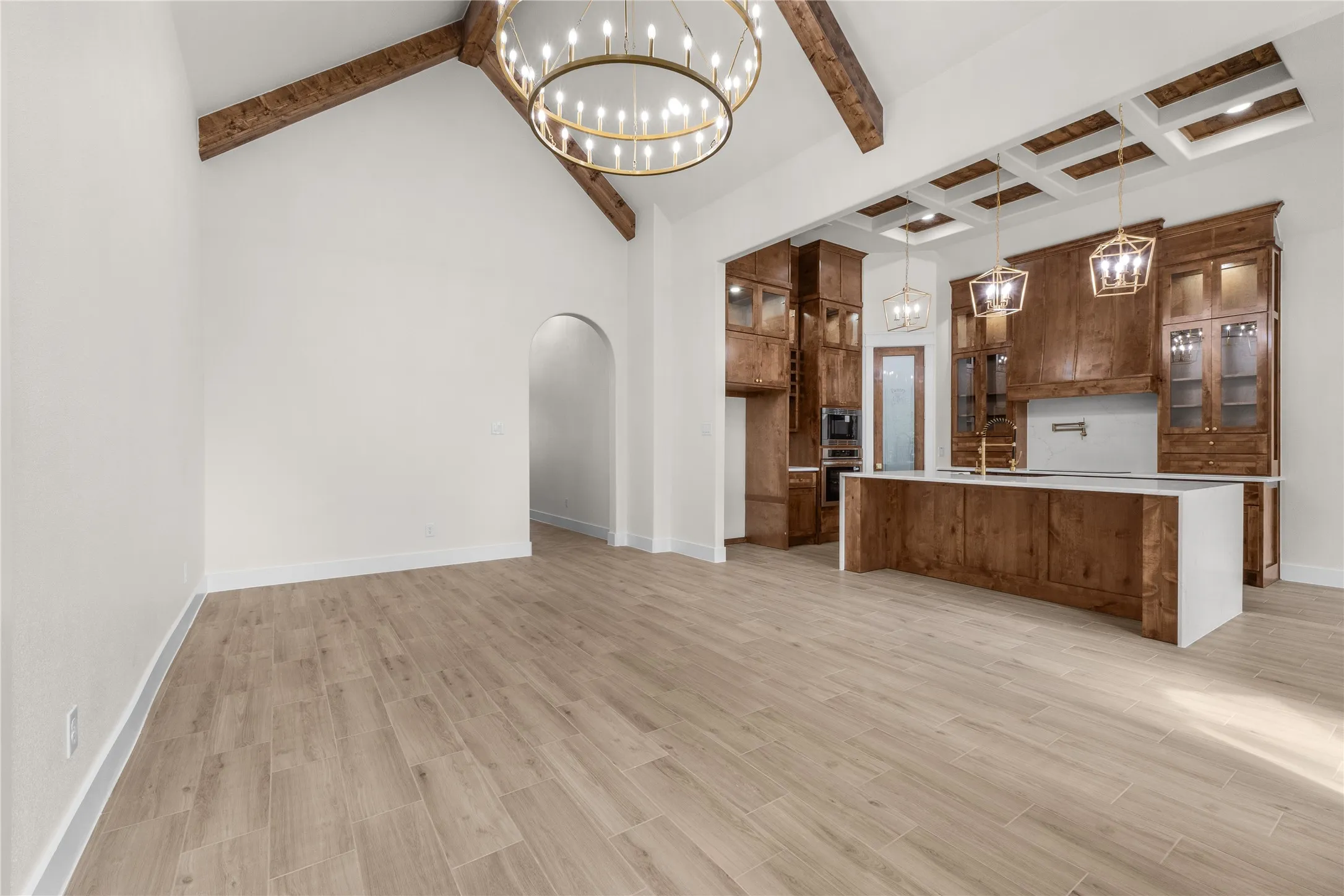 Vaulted ceiling with exposed wood beams, wood-finish tile flooring, custom cabinetry, kitchen island with stone countertop, and coffered ceiling detail