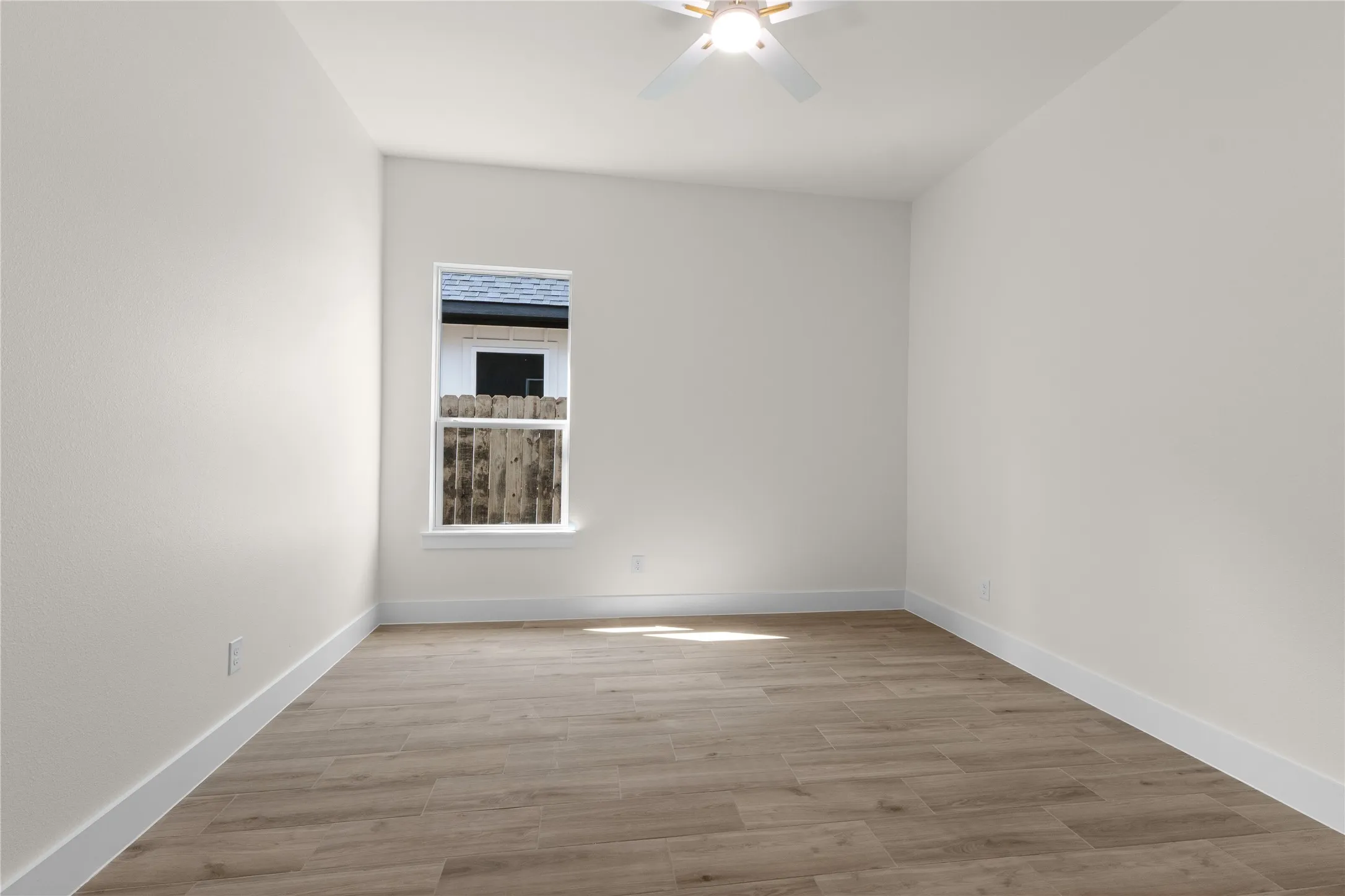 Interior space featuring wood-finish flooring, crisp neutral wall paint, and a white ceiling fan with integrated lighting
