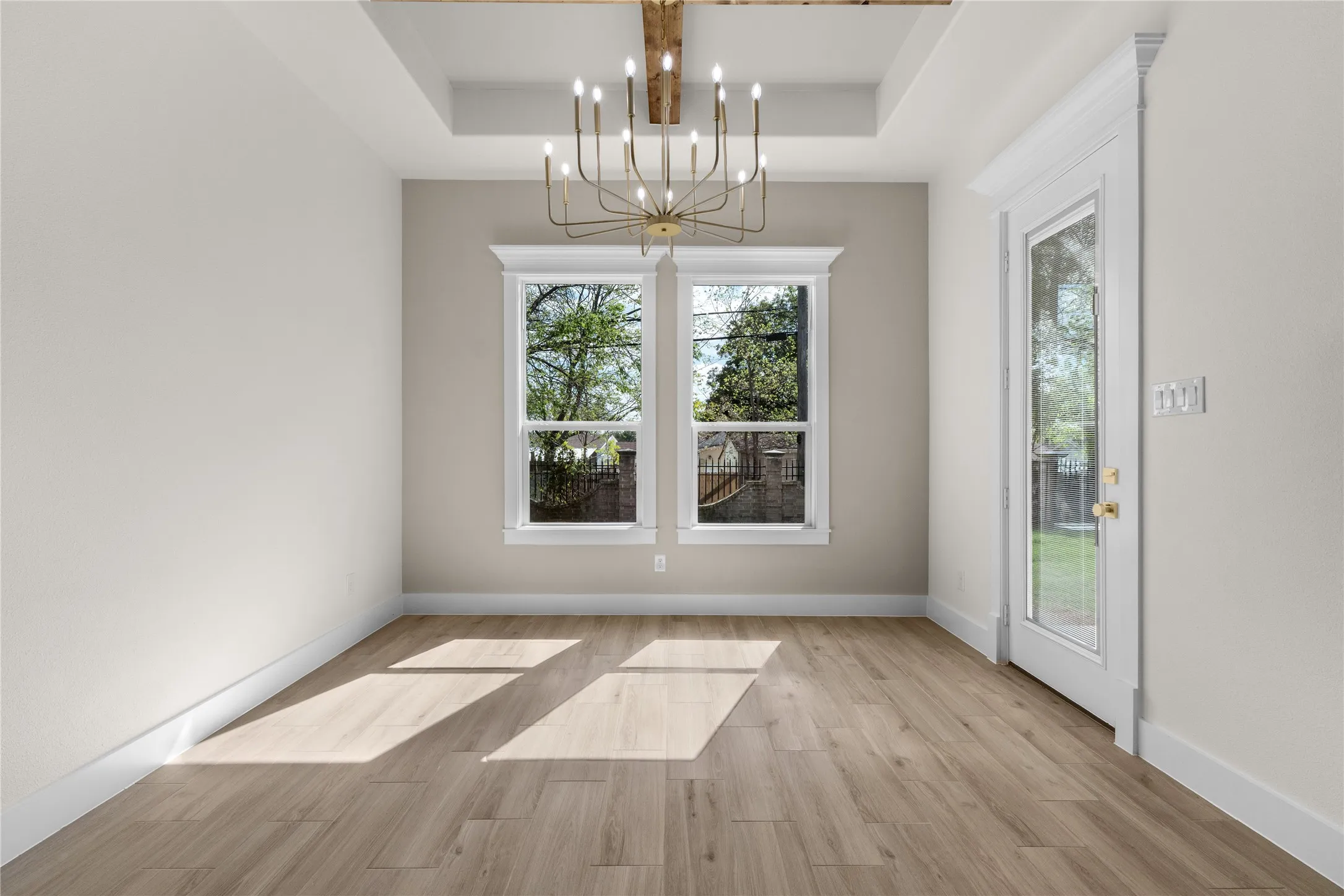 Tray ceiling featuring a stained wood beam, complemented by a multi-arm chandelier, wood-finish flooring, and a glass-paneled exterior door