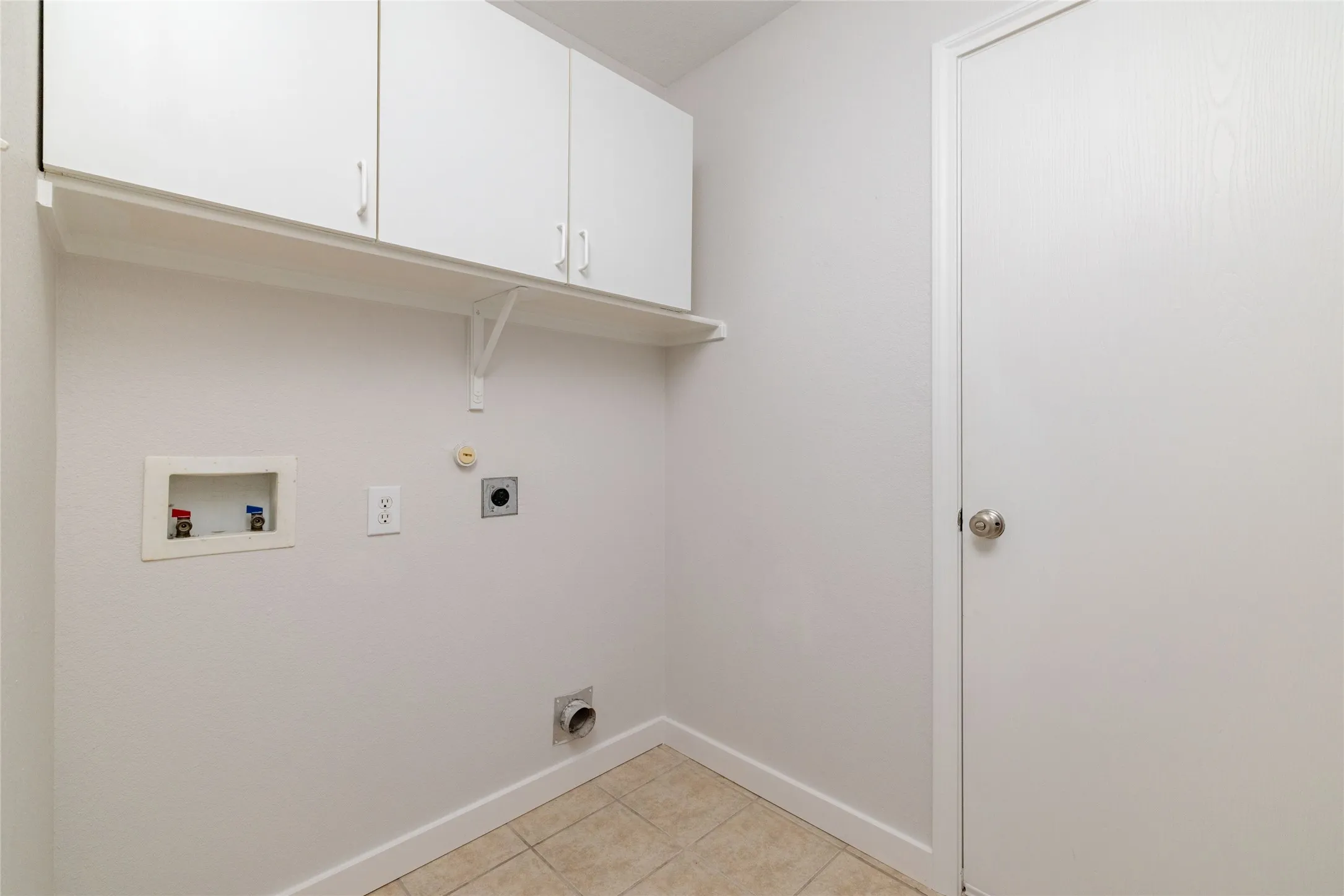 Utility space featuring wall-mounted white cabinetry, open shelving, tile flooring, and a solid-core interior door
