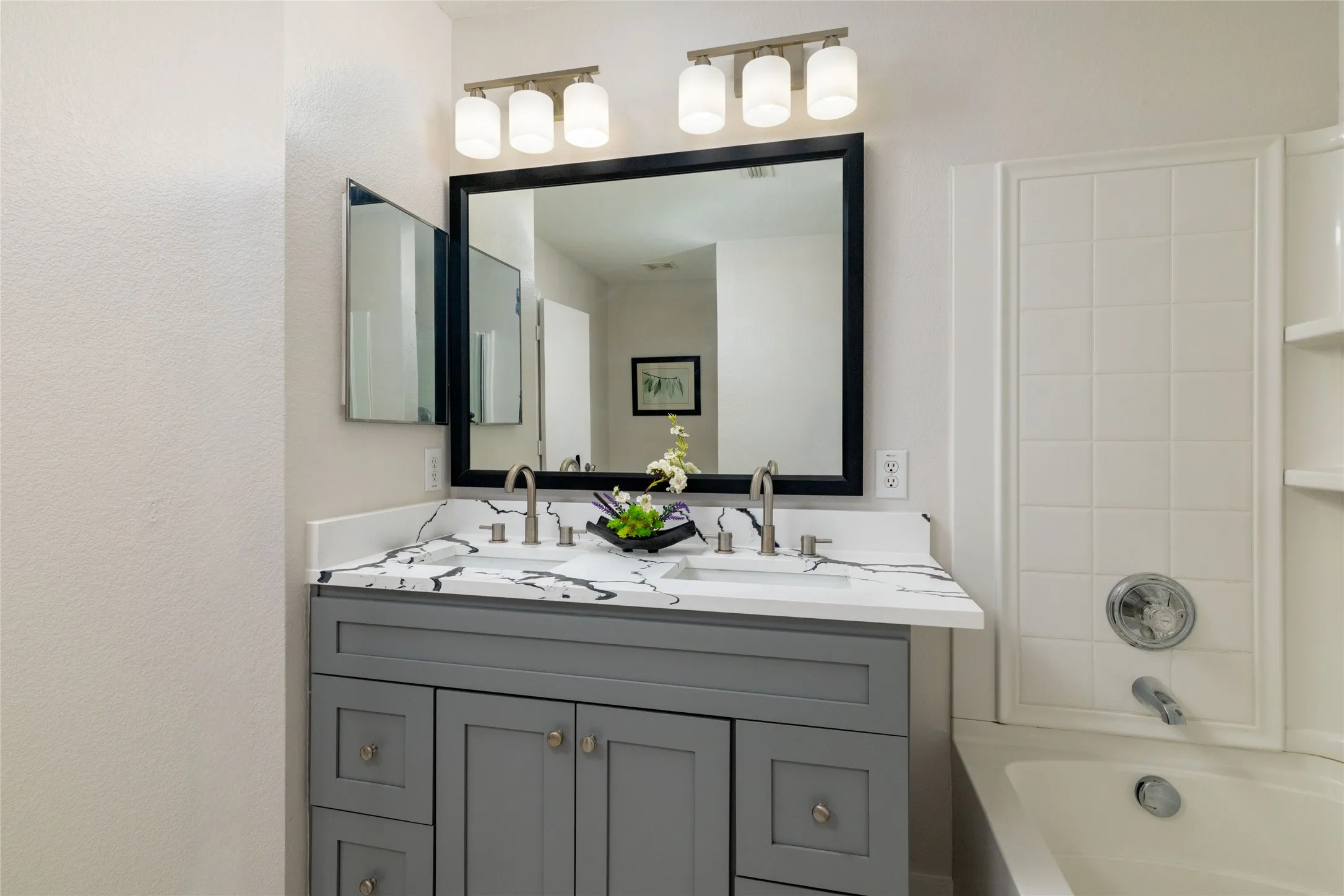 Grey shaker-style dual vanity with a white-and-grey veined countertop, dual undermount sinks, polished nickel faucets, and a framed vanity mirror with dual glass light fixtures