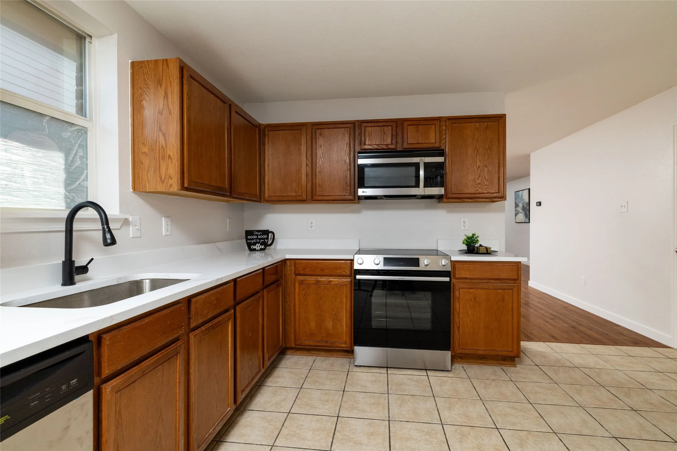 Kitchen featuring wood cabinetry, white countertops, stainless steel appliances, a matte black faucet, and tile flooring