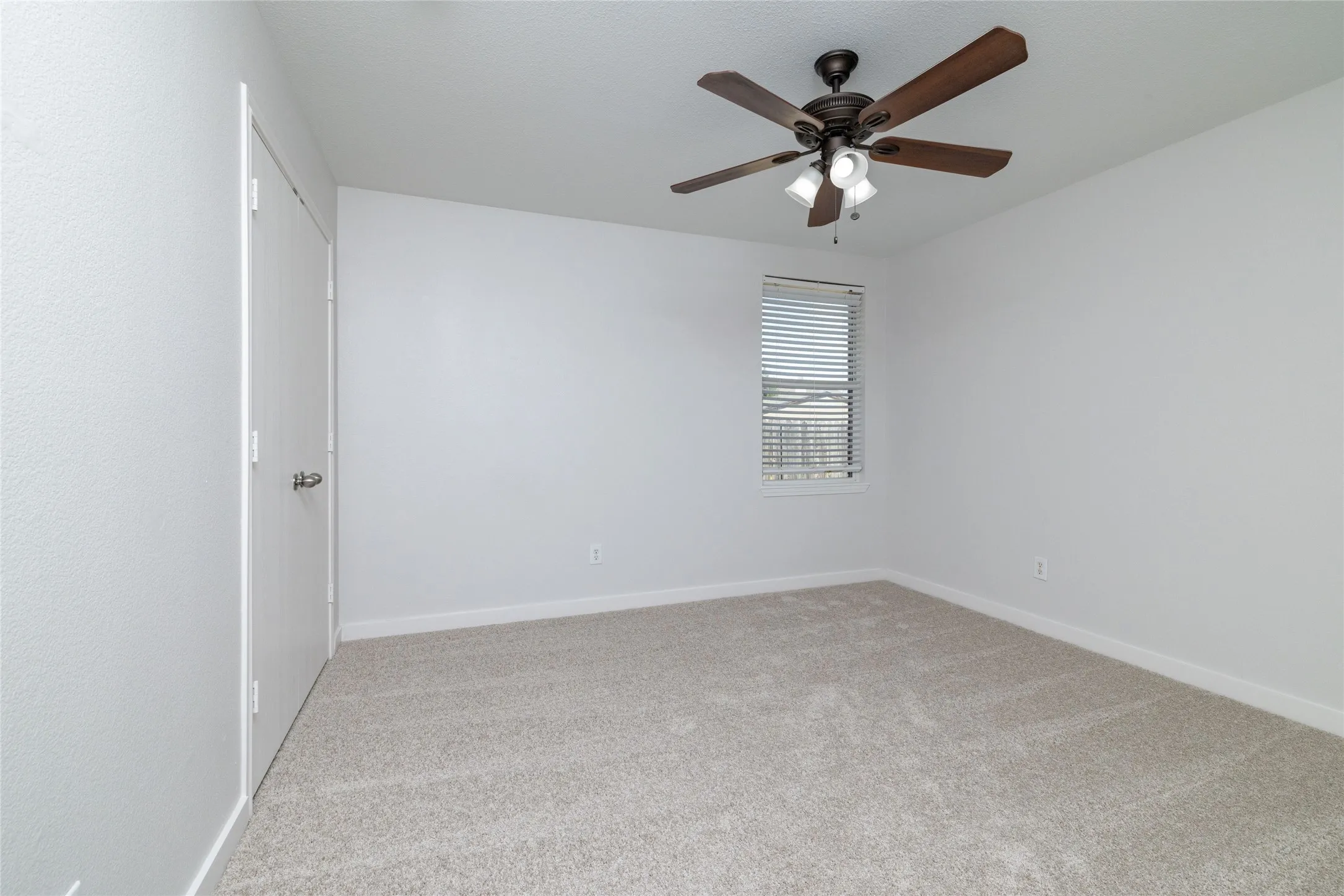 Neutral interior featuring wall-to-wall carpeting, a multi-blade ceiling fan with integrated lighting, and a single-pane window with horizontal blinds