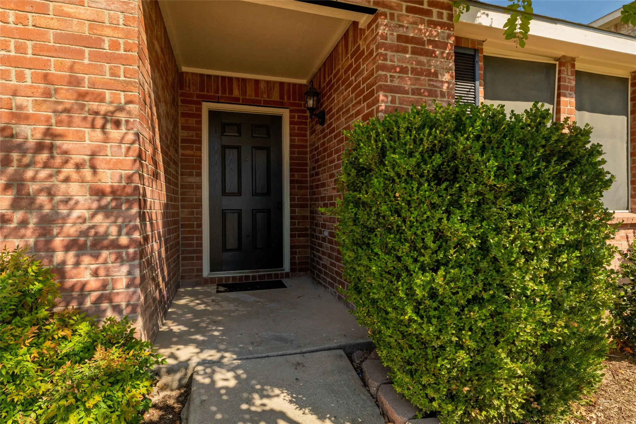Brick exterior entry featuring a six-panel front door, covered porch, and integrated exterior light fixture
