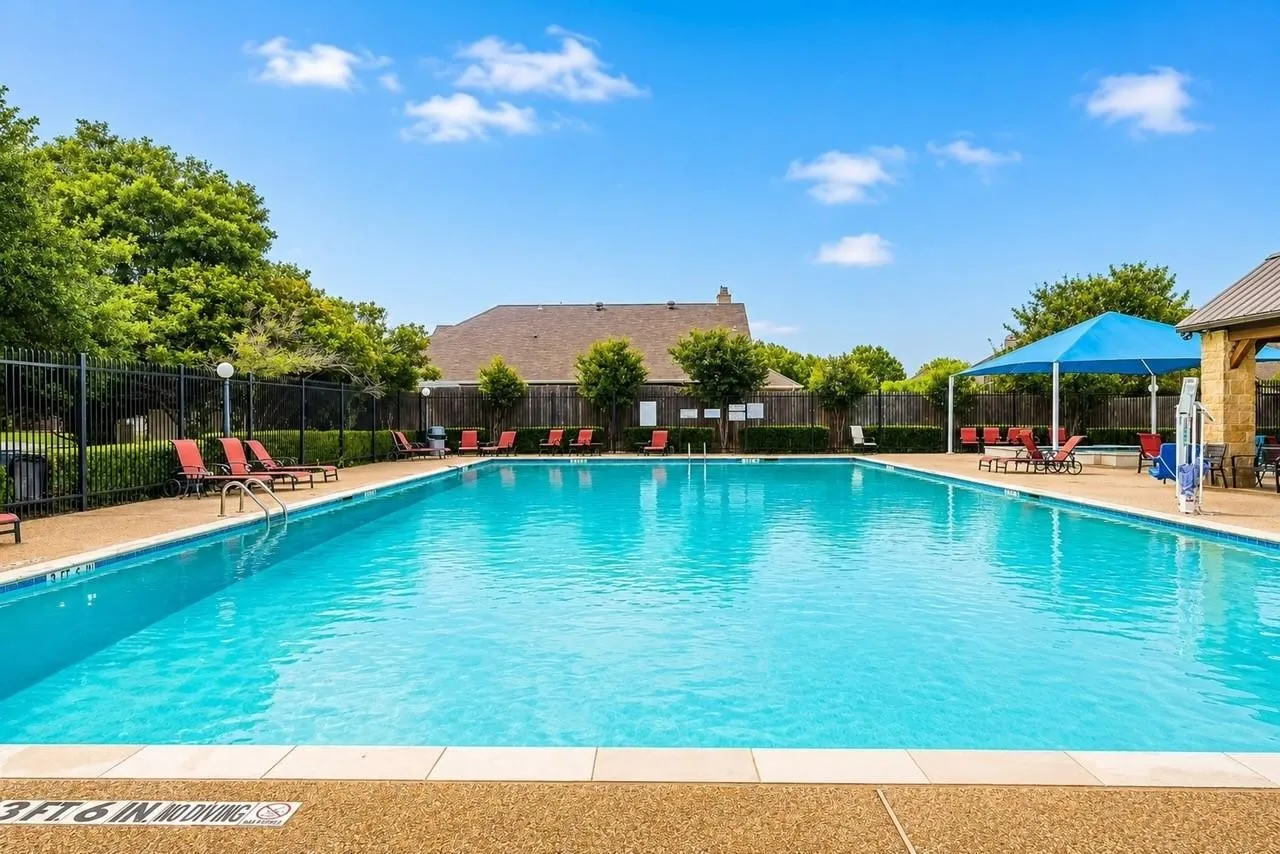 Community swimming pool featuring a concrete deck, metal perimeter fencing, and a shaded pavilion