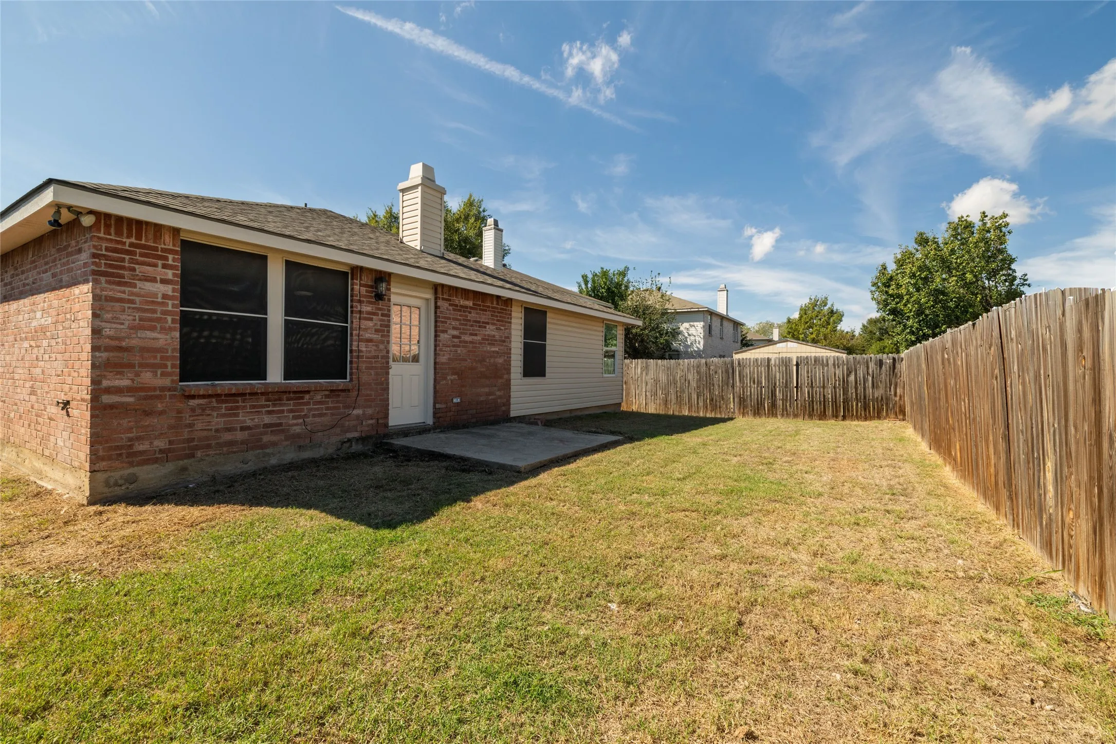 Rear exterior featuring brick and horizontal siding, concrete patio, two chimneys, and perimeter wood fencing