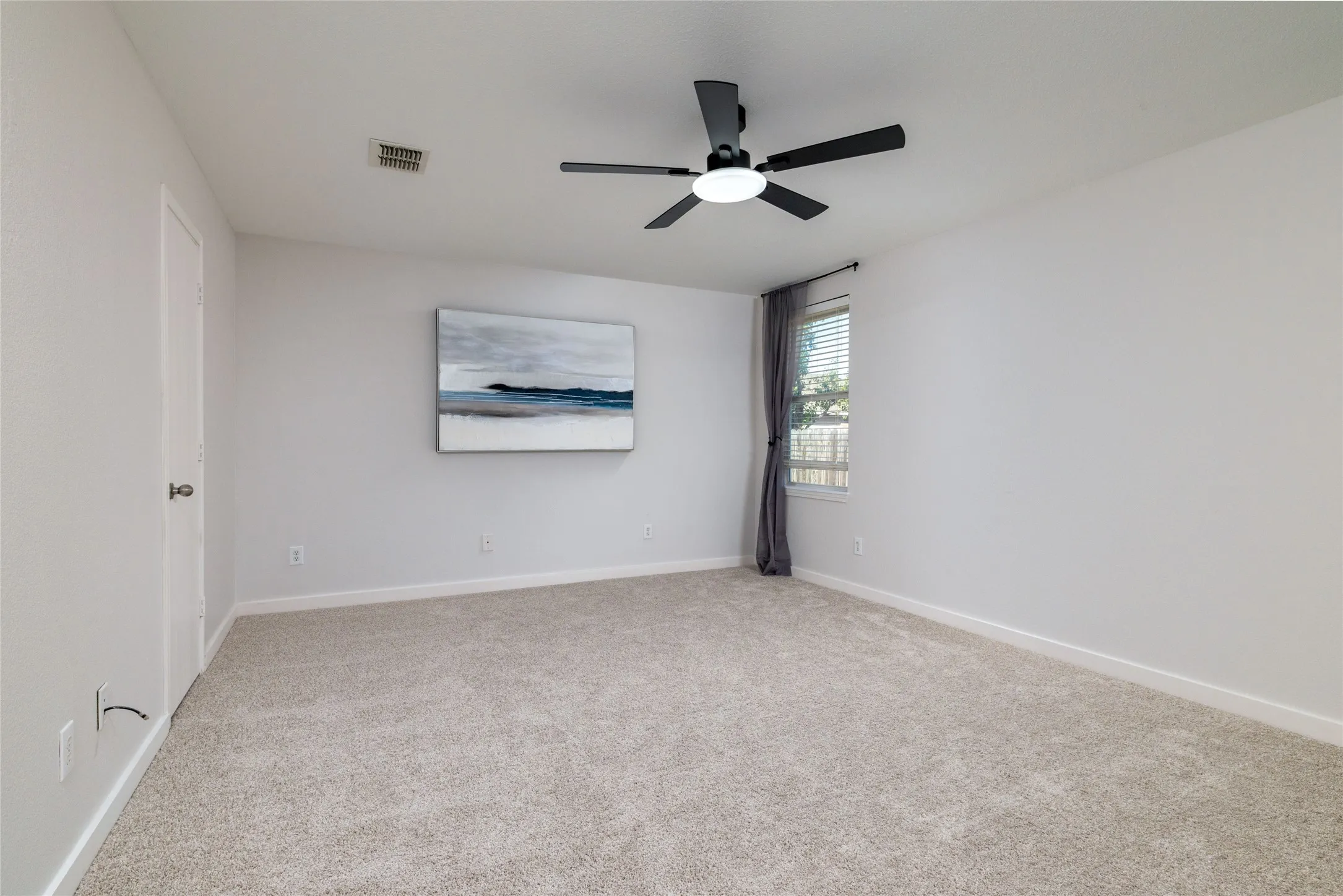Neutral-toned interior space featuring light-colored wall-to-wall carpeting, a matte black multi-blade ceiling fan with integrated lighting, and a single-pane window