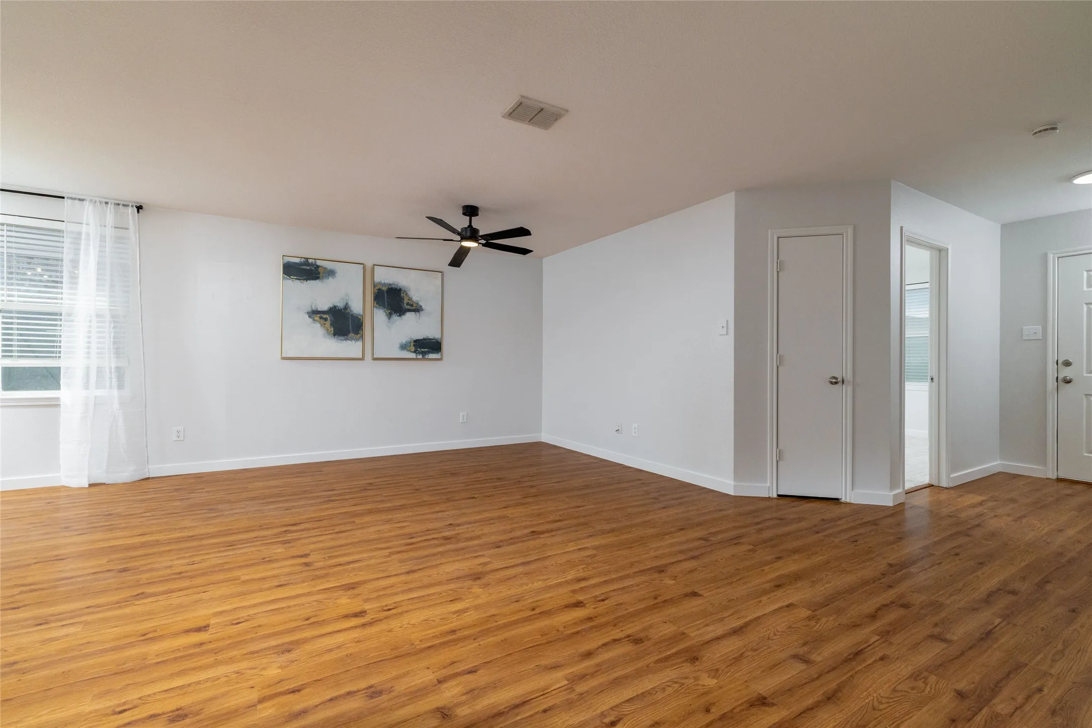 Open floor plan featuring wood-finish flooring, neutral wall paint, and a ceiling-mounted fan with integrated lighting
