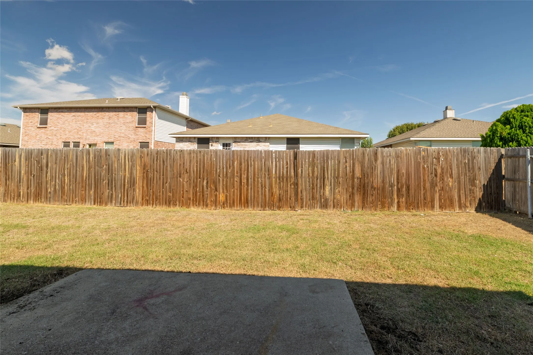 Fenced backyard featuring a concrete patio and a lawn
