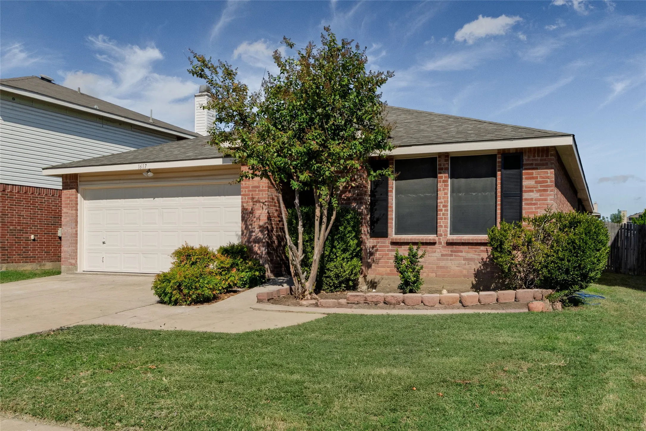 Single-story residence featuring a brick exterior, attached two-car garage, multi-paneled garage door, and decorative window shutters