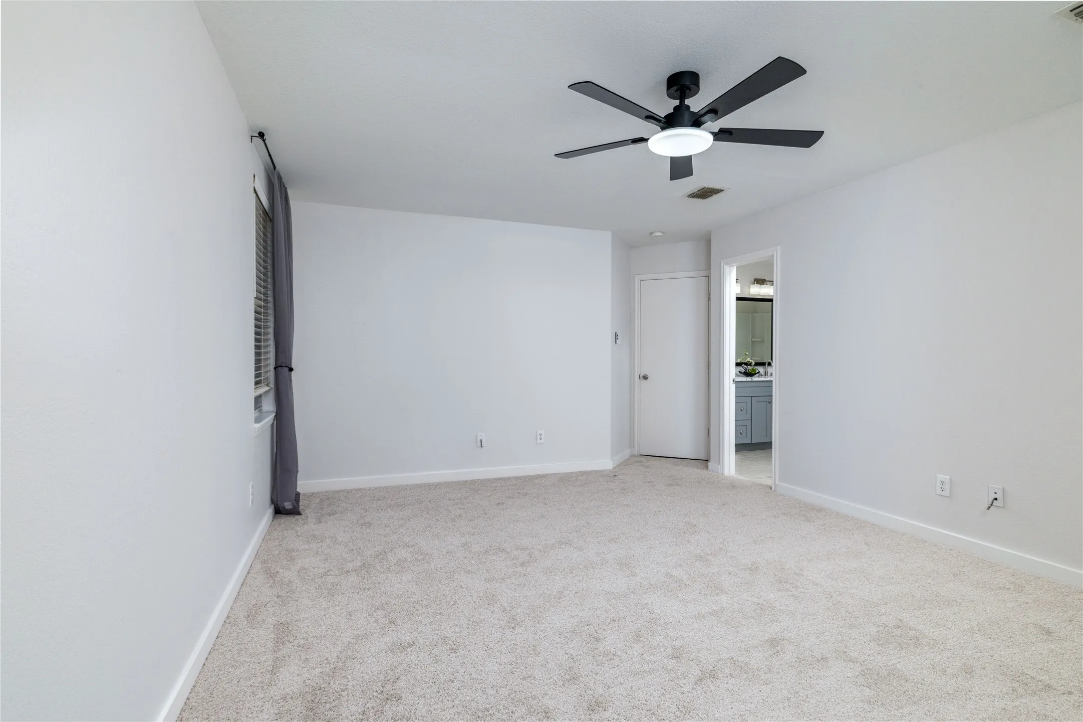 Interior room featuring neutral wall-to-wall carpeting, a matte black multi-blade ceiling fan with integrated LED lighting, and a doorway opening to a secondary space