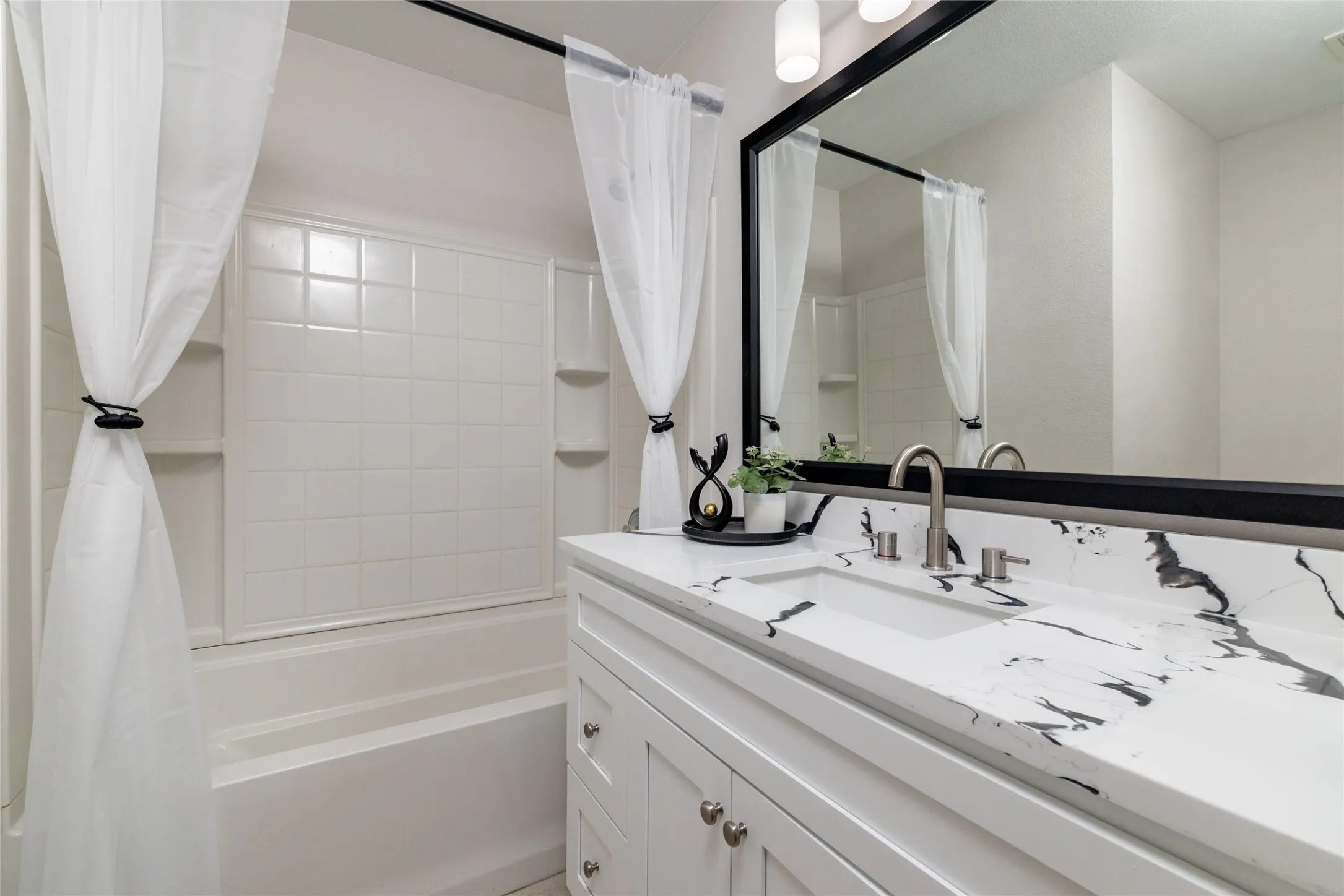 Bathroom featuring a white vanity with a patterned stone countertop, integrated sink, matte black-framed mirror, and a tub-shower combination with a tiled surround