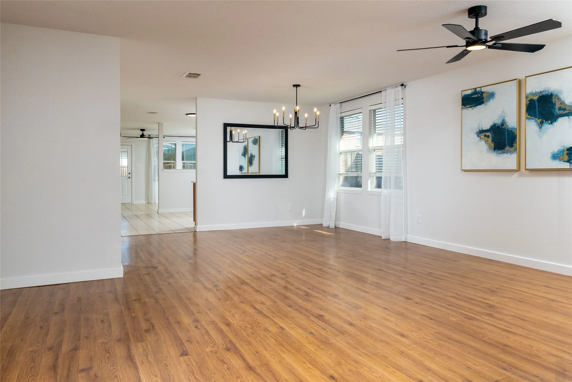 Open living area featuring wood-finish flooring, a multi-arm chandelier, and a matte black ceiling fan with integrated lighting
