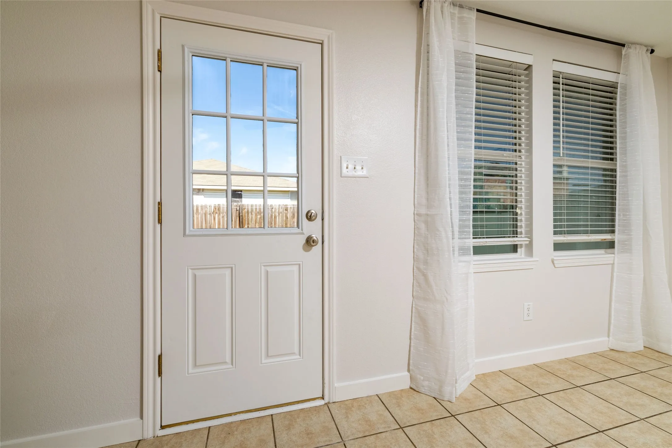 Exterior door featuring a nine-lite glass insert, dual windows with horizontal blinds, and neutral-toned tile flooring