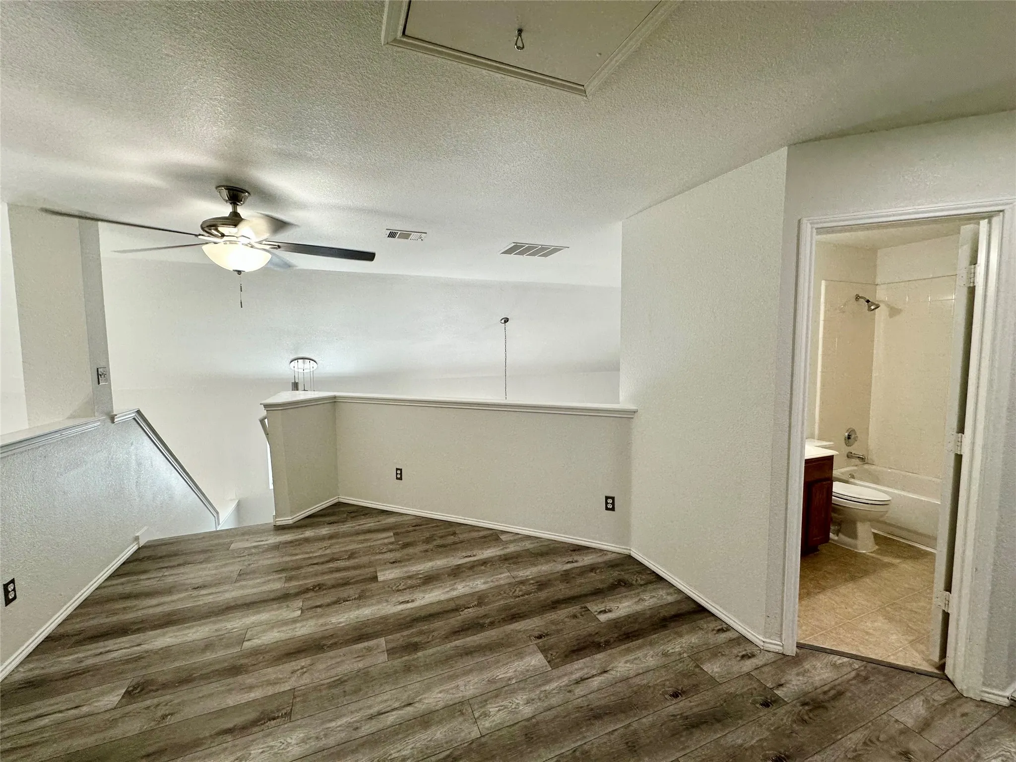 Open loft area featuring wood-finish flooring, ceiling fan with integrated lighting, and access to a full bathroom with a combination tub and shower