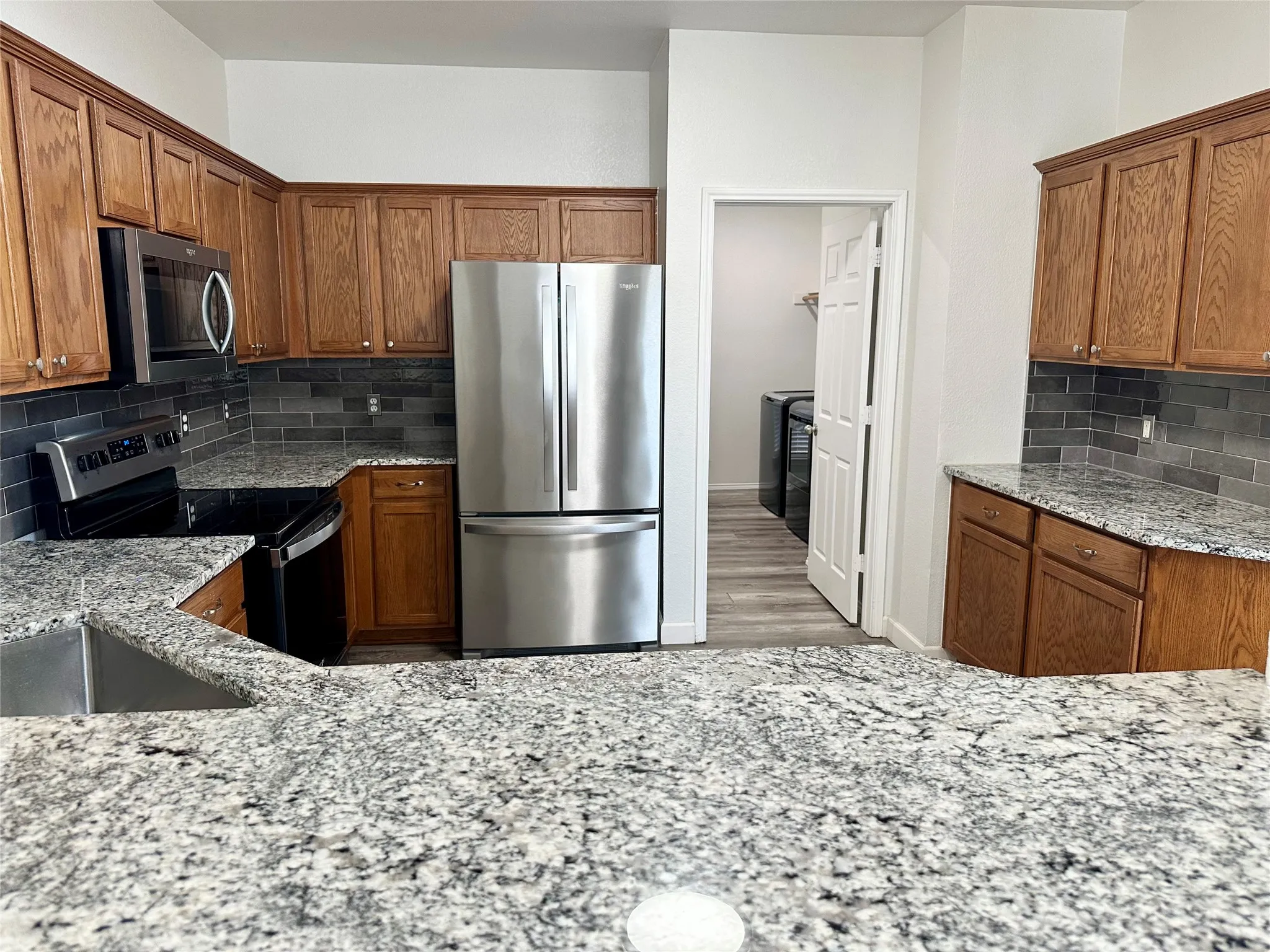 Kitchen featuring wood cabinetry, stone countertops, dark rectangular tile backsplash, stainless steel appliances, and integrated microwave