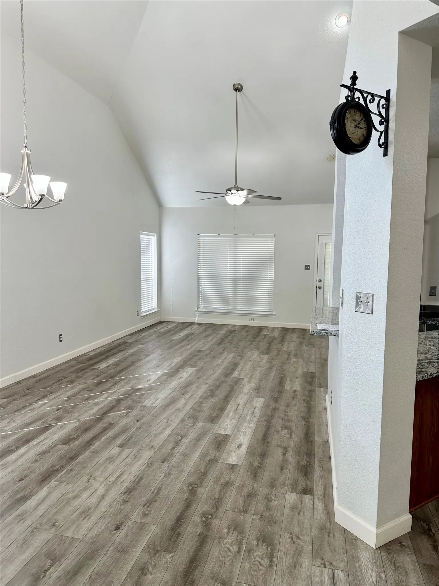 Vaulted ceiling featuring a central ceiling fan with integrated light, wood-finish flooring, and multi-arm chandelier lighting